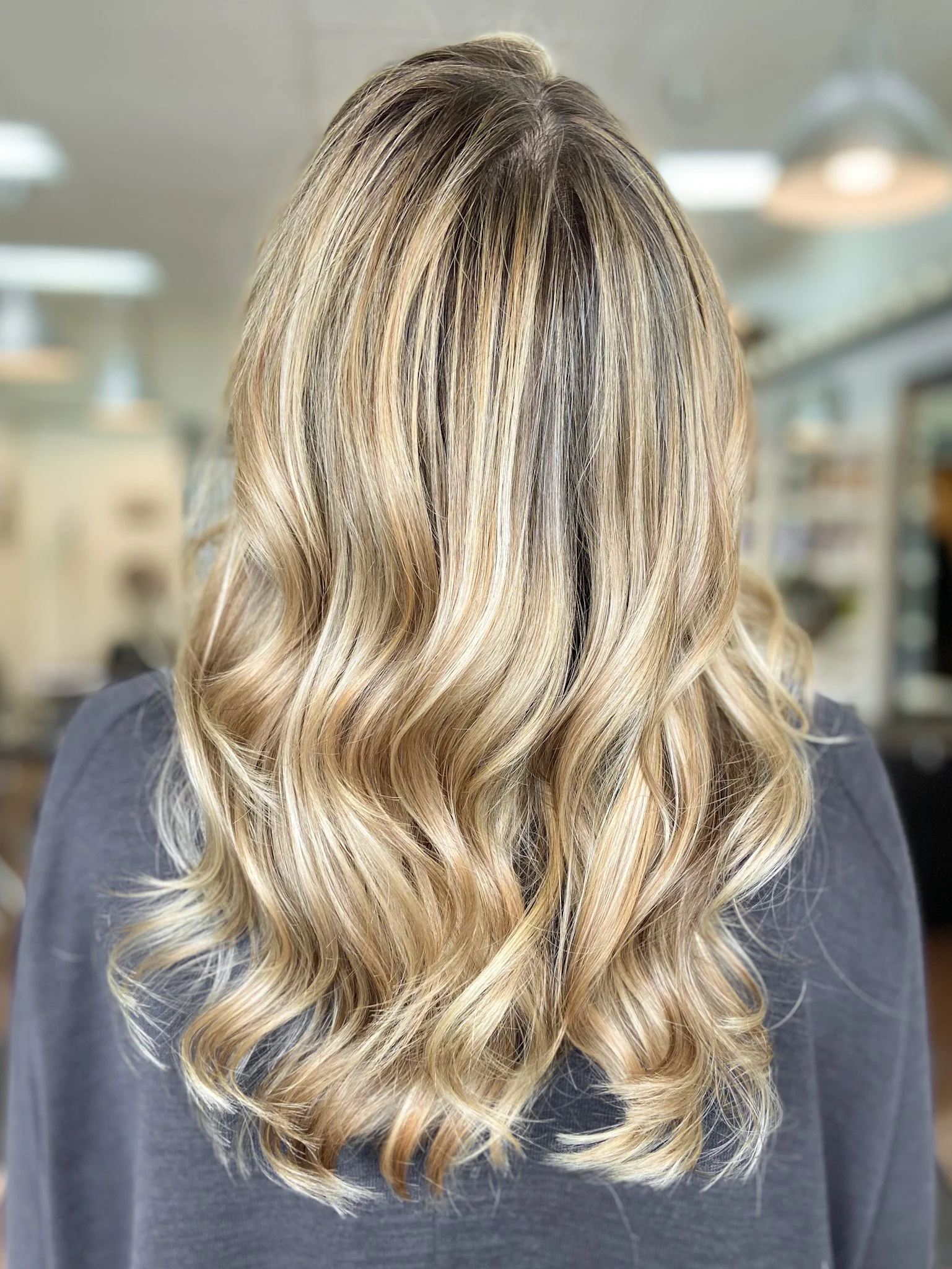 Back view of a woman's blonde, wavy hair in a salon setting.