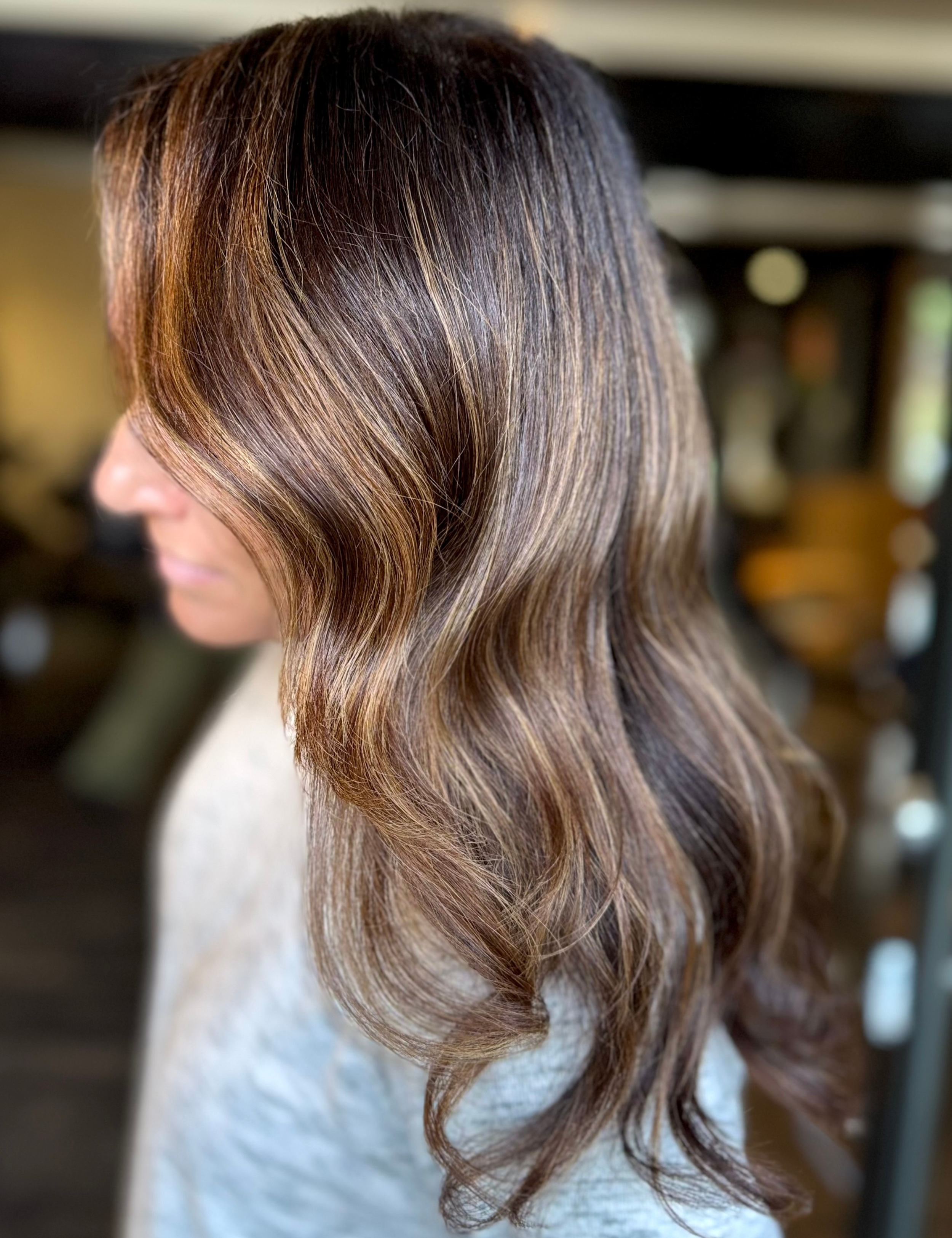 Woman with long, wavy, brown hair with highlights, viewed from the side.
