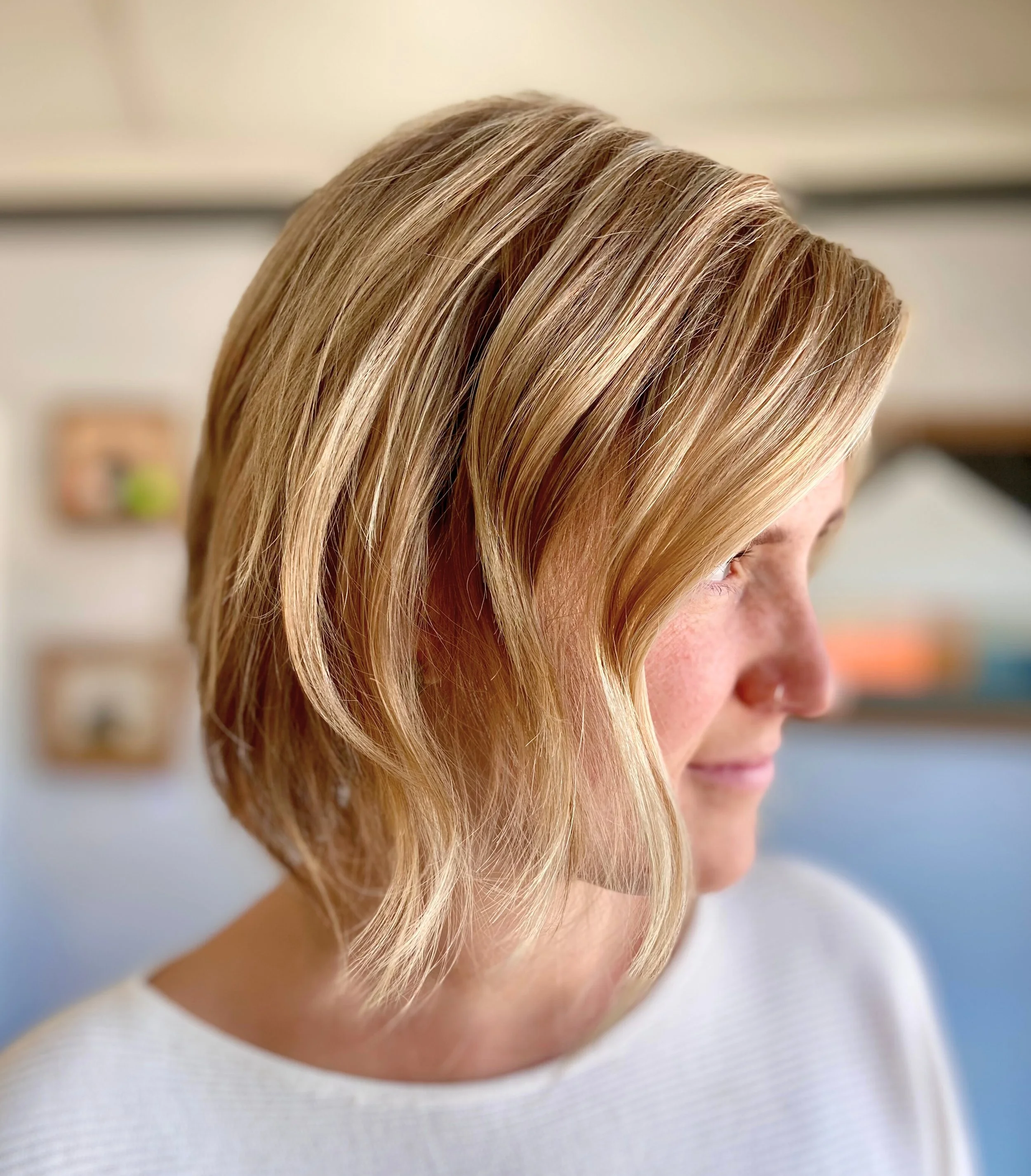 Profile of a woman with blonde, wavy, shoulder-length hair wearing a white top.
