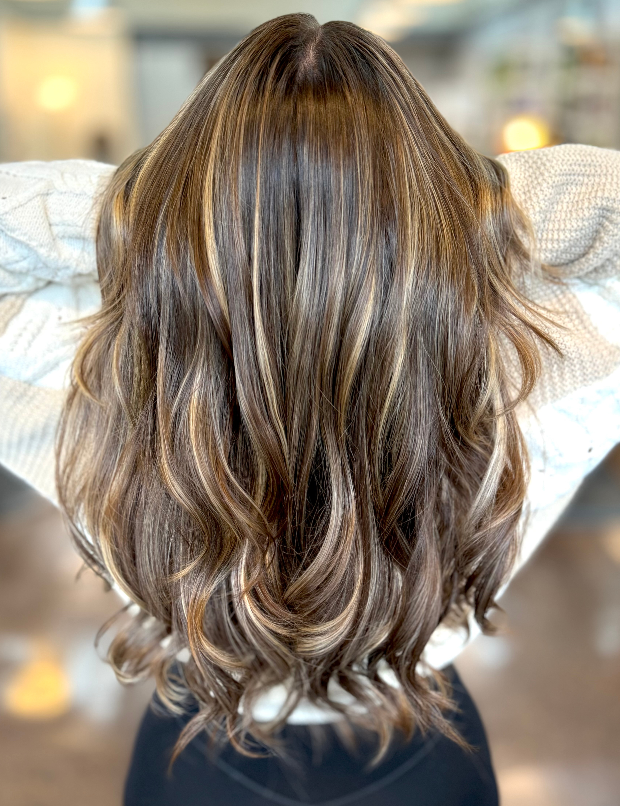 Close-up of a woman's long, wavy hair with highlights, viewed from behind.