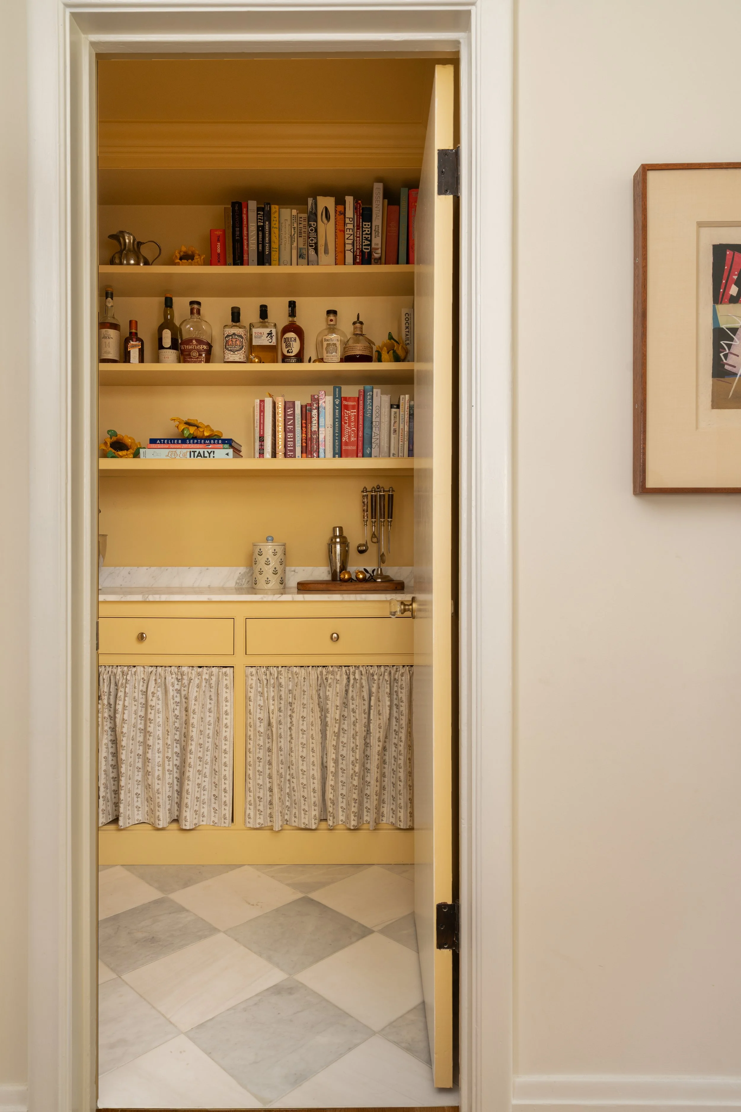 View into yellow pantry with marble checkerboard floor and whimsical curtains.