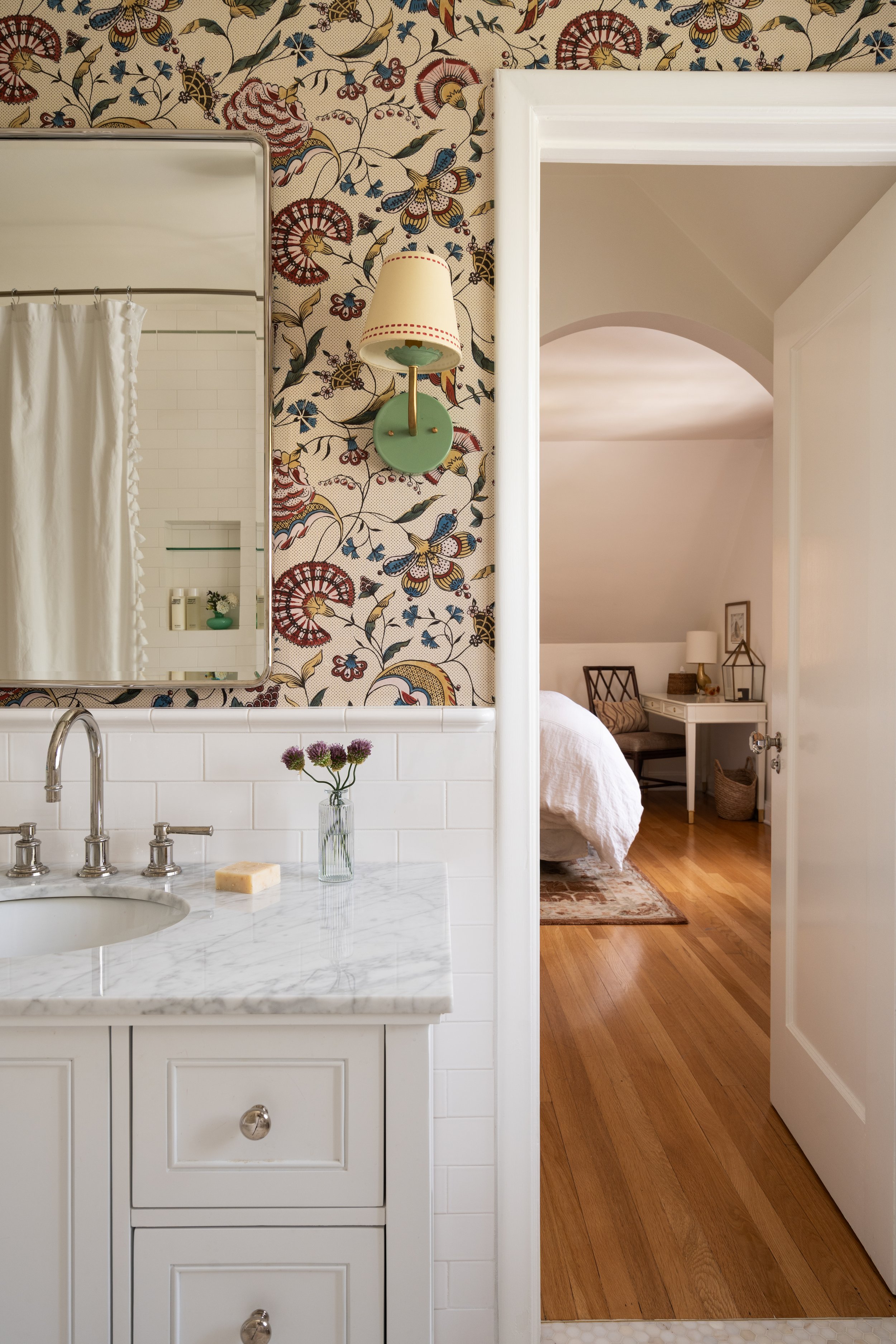 Kids bathroom with playful wallpaper, green sconce, and marble topped vanity.