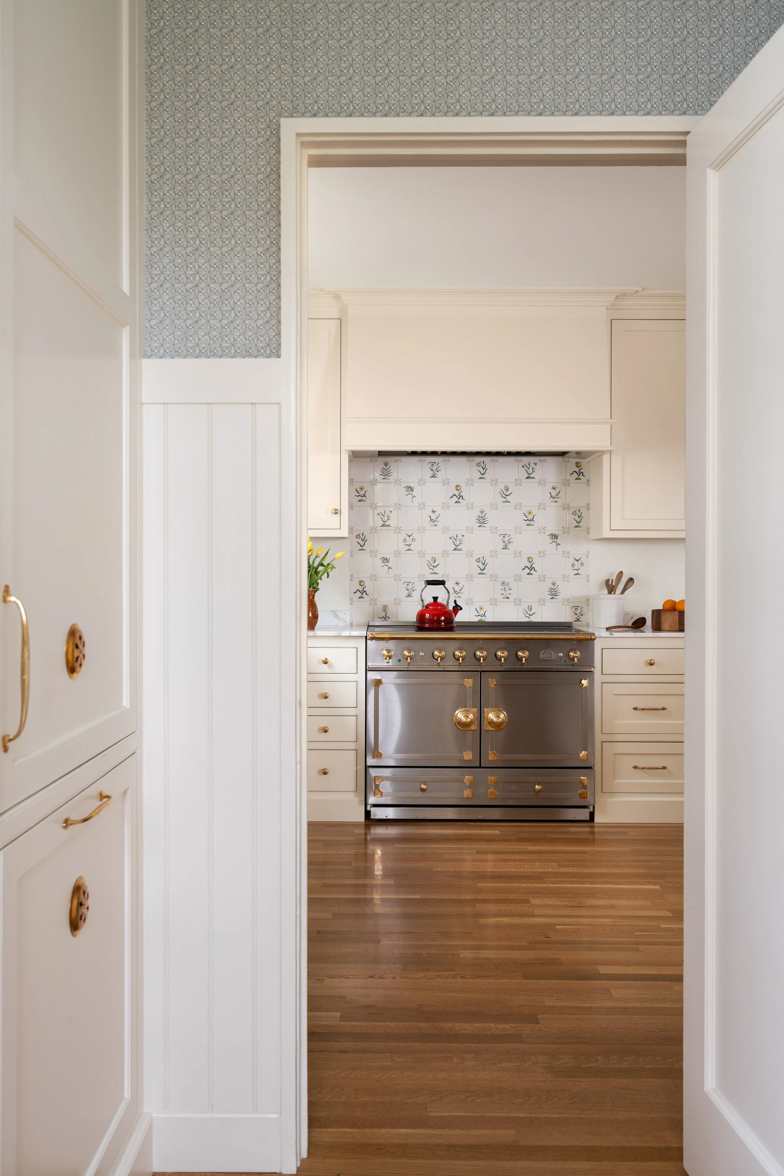 Glimpse into a La Cornue range and handpainted tile backsplash from a tonge and groove paneled laundry room.