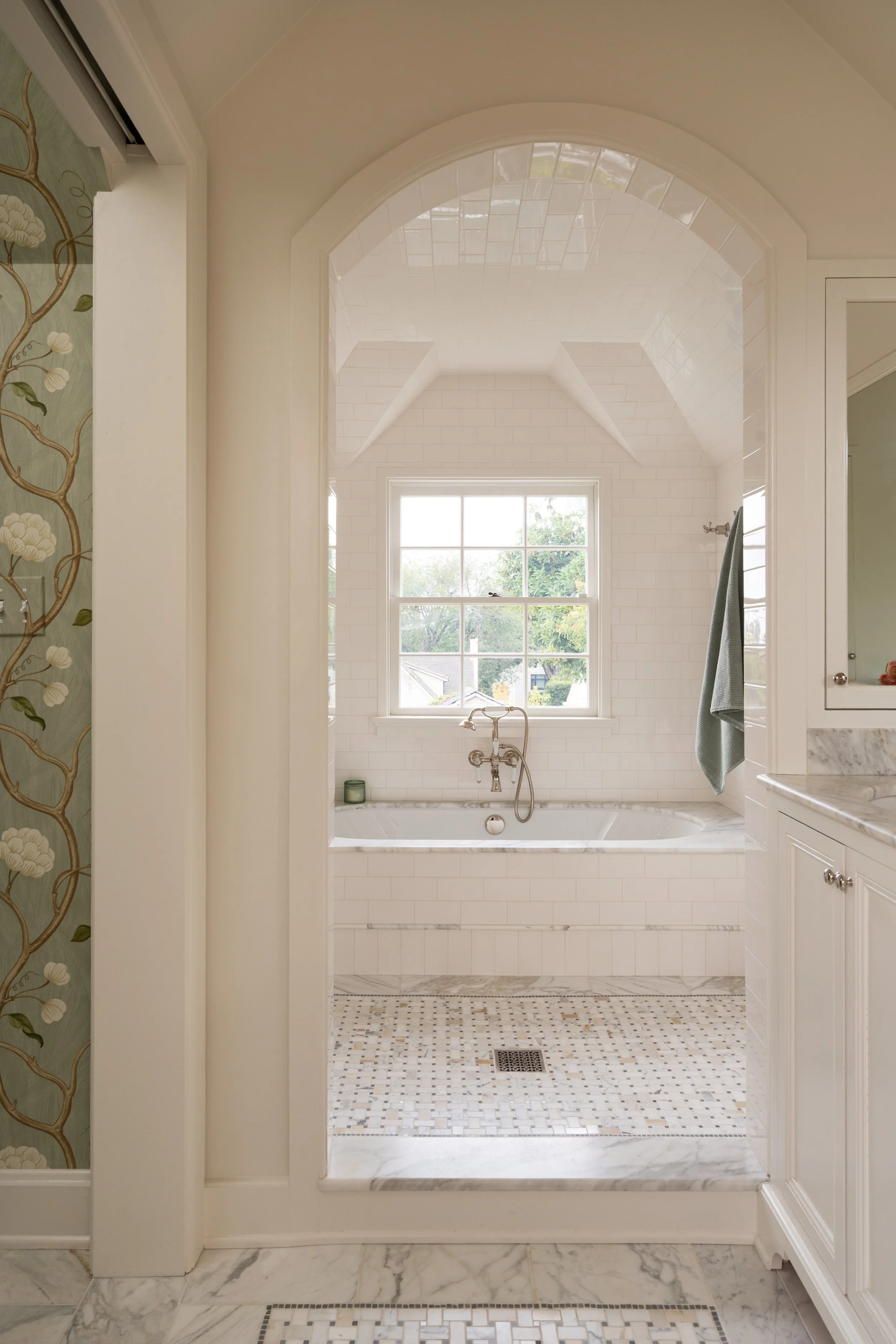 Floral wallpaper peak into oval tub with marble tub deck and custom marble inset floor.