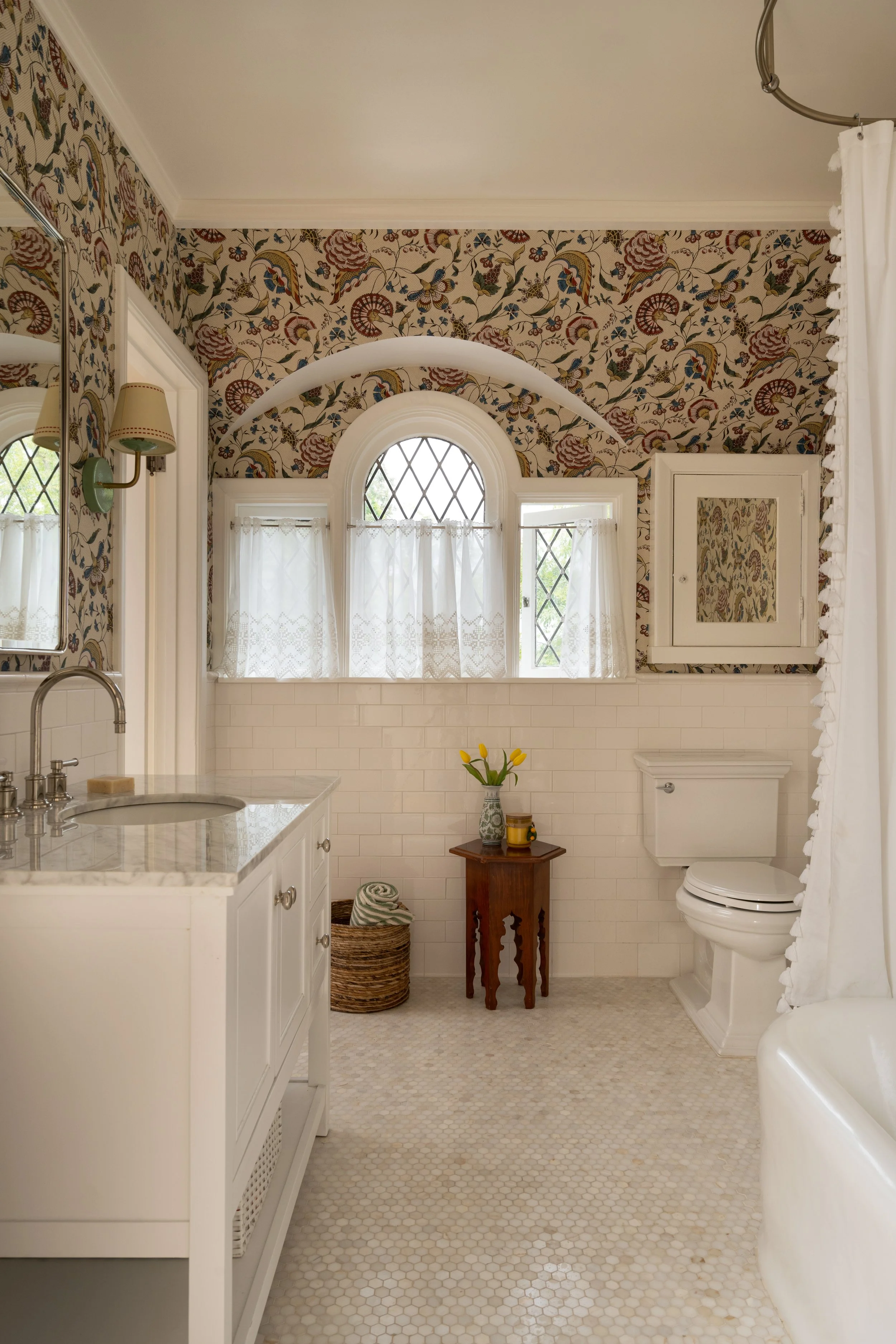 Subway tile wainscot with playful wallpaper decorate this kids bath with classical detailing and marble mosaic floor.