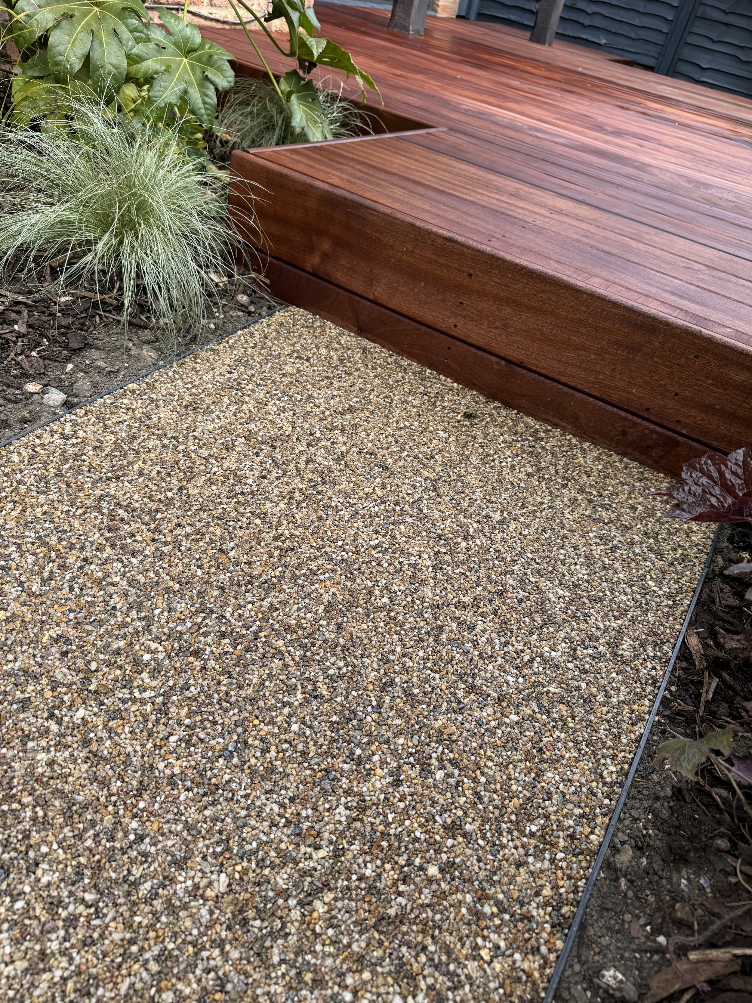 Wooden deck with steps next to gravel path and plants.