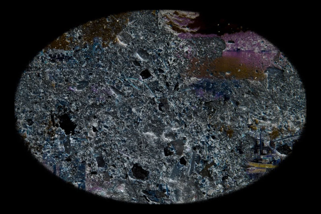 A close-up of a textured, circular surface with various colors and embedded small objects, surrounded by a black background.