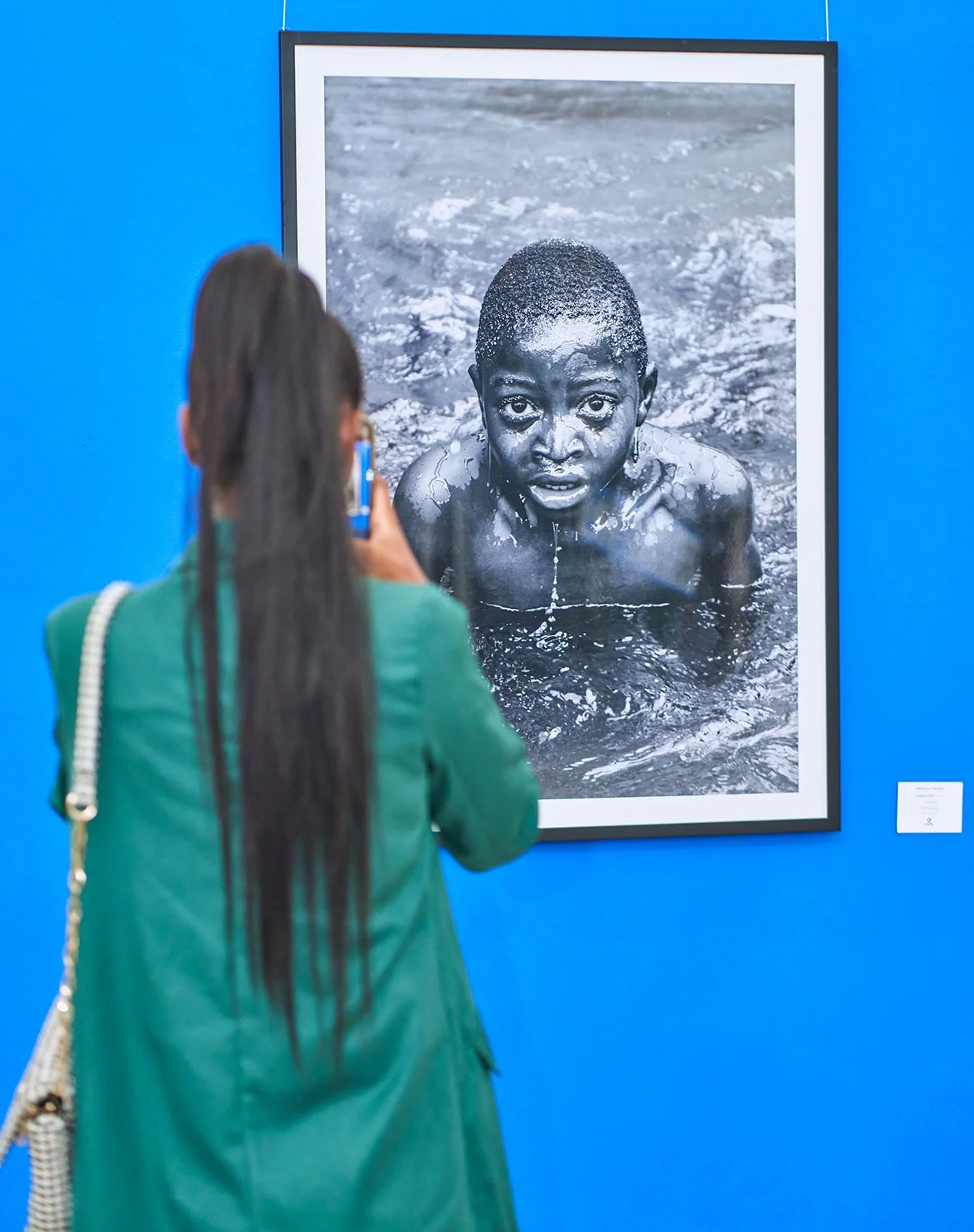 Photo of woman in green clothes taking a photo of a piece of black and white art on a blue wall
