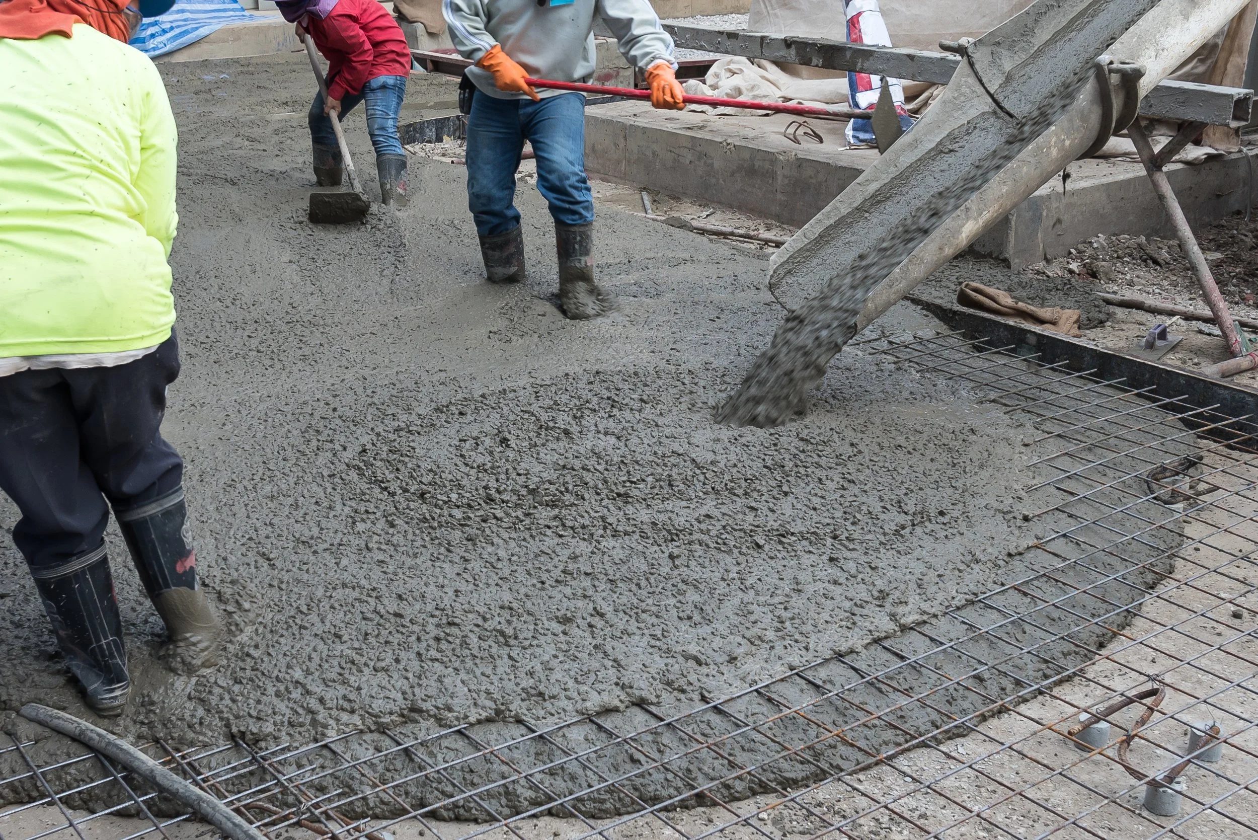 Workers pouring concrete over rebar at a construction site.