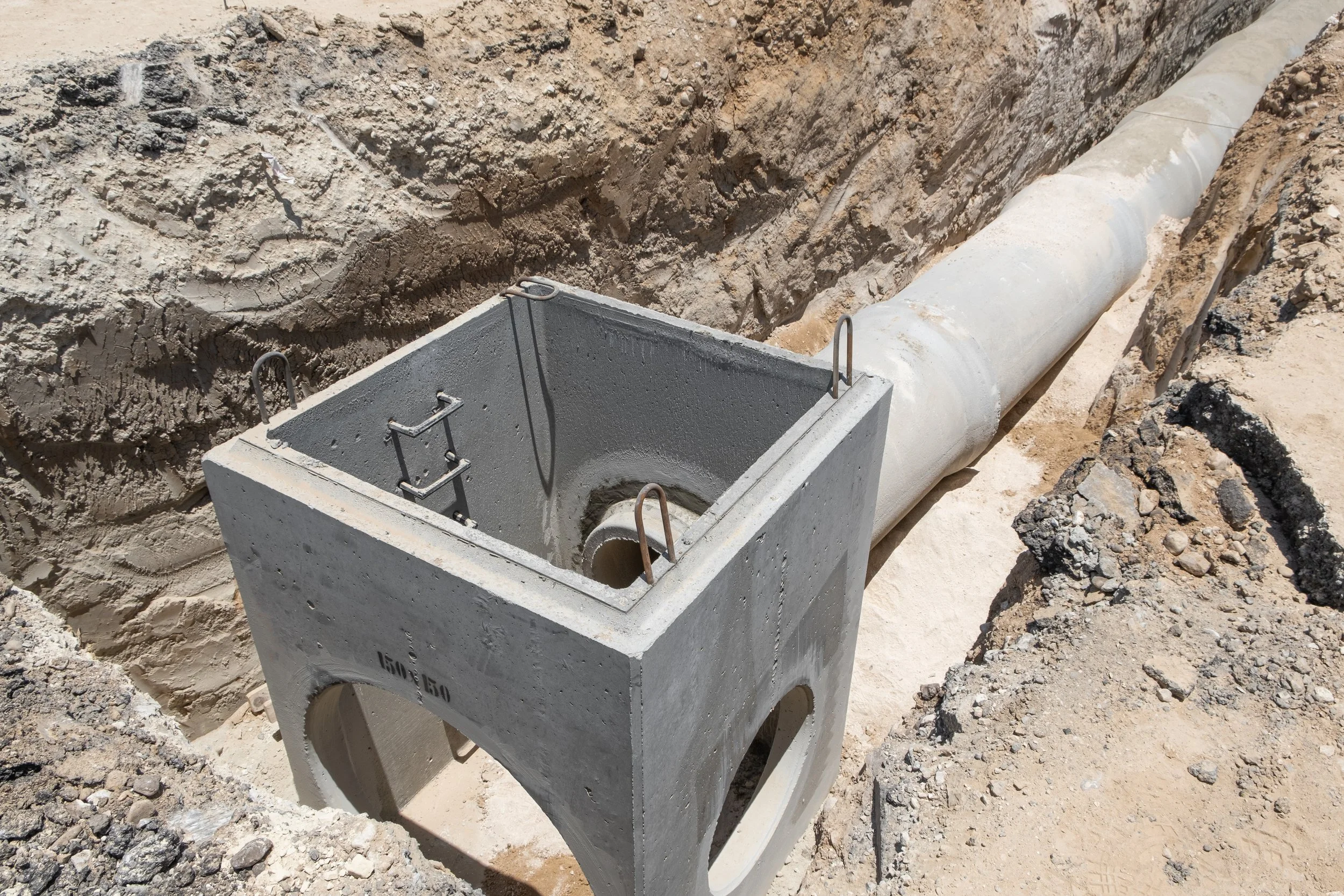 Underground concrete utility manhole with large pipeline in trench for infrastructure construction.