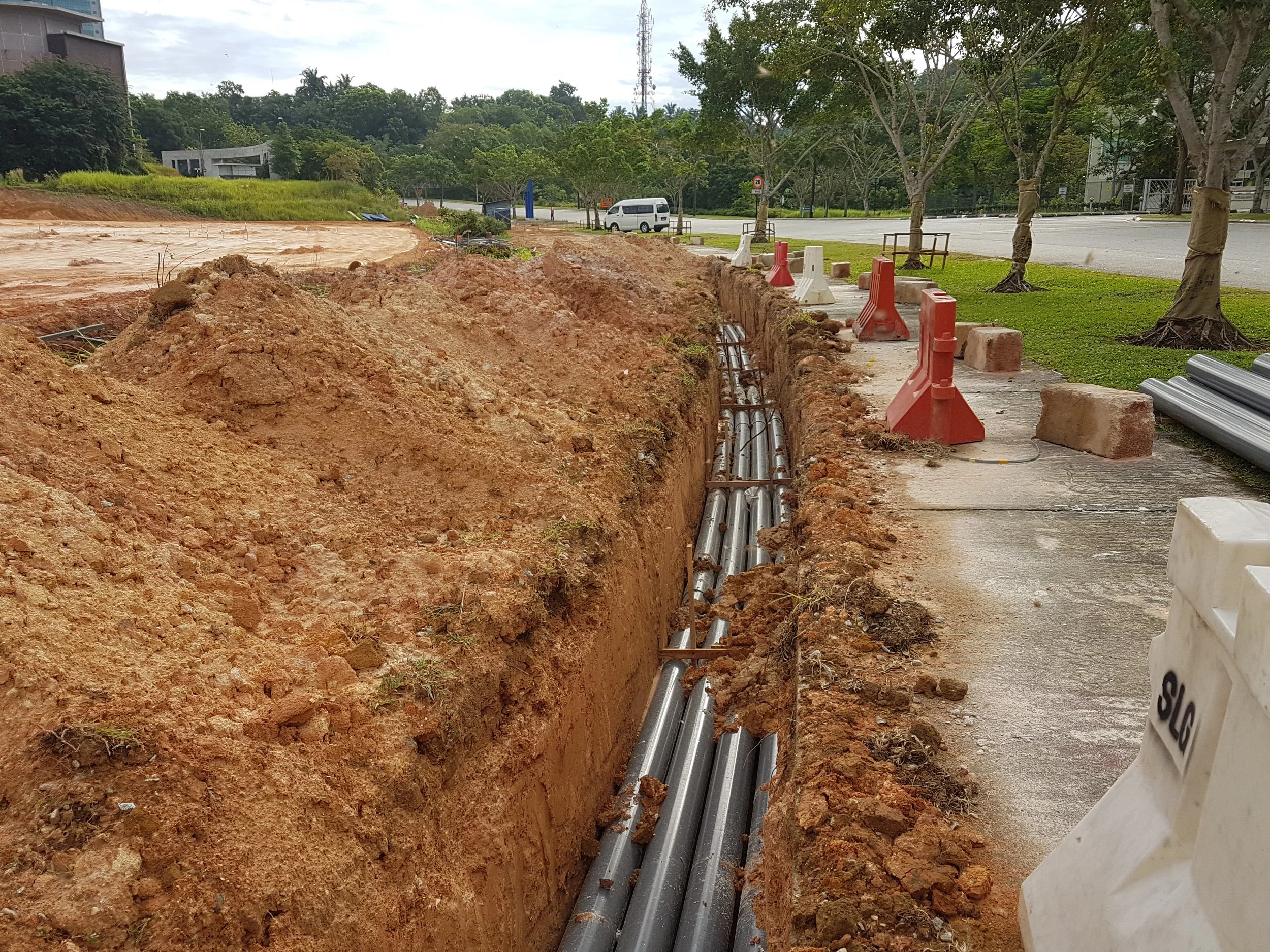 Trench with underground pipes and traffic barriers at a construction site.