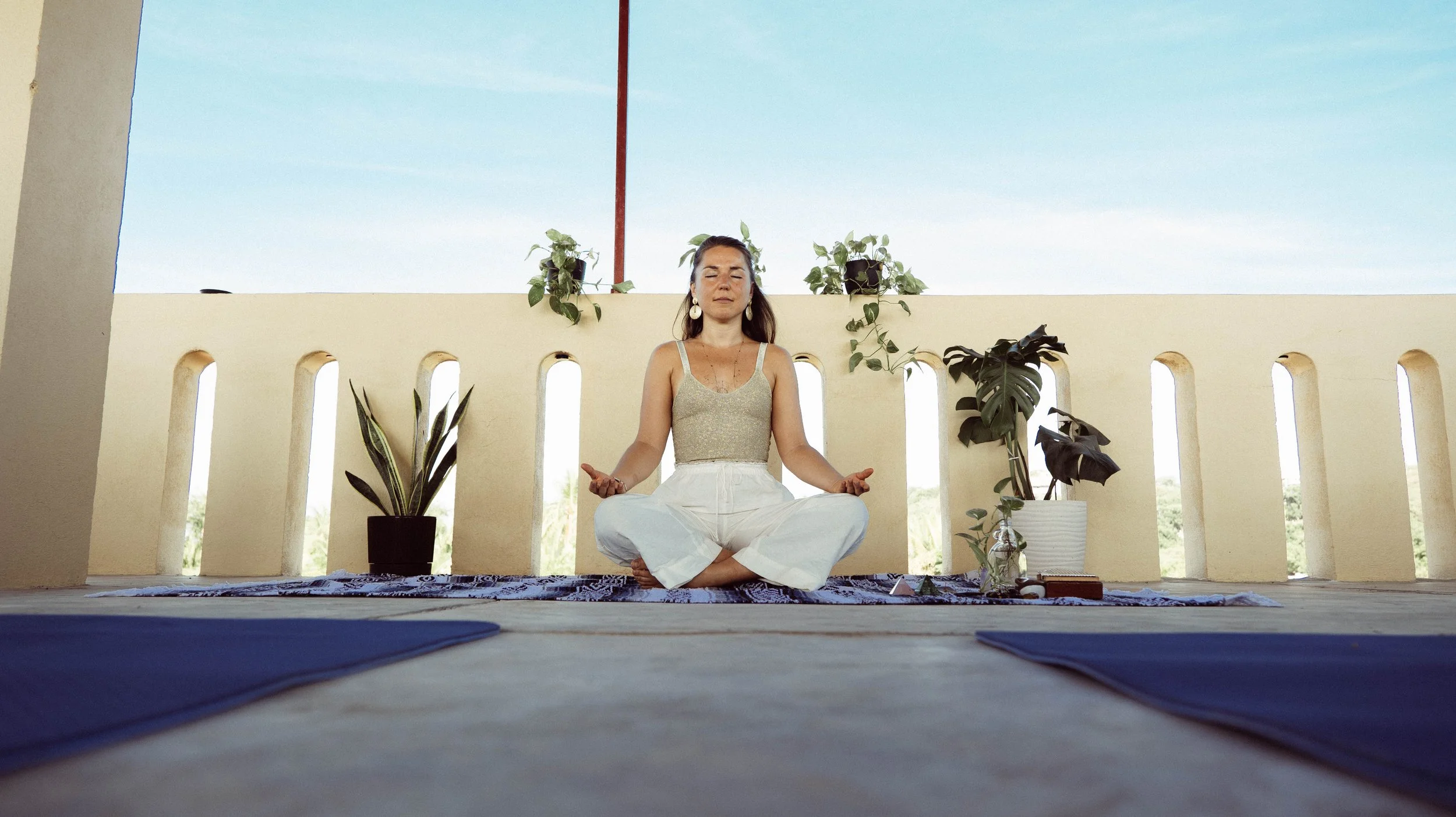 A woman outdoors wearing a gray turtleneck sweater, with long brown hair, holding her hands over her chest. She is wearing a beaded bracelet, a ring, and a pendant necklace.