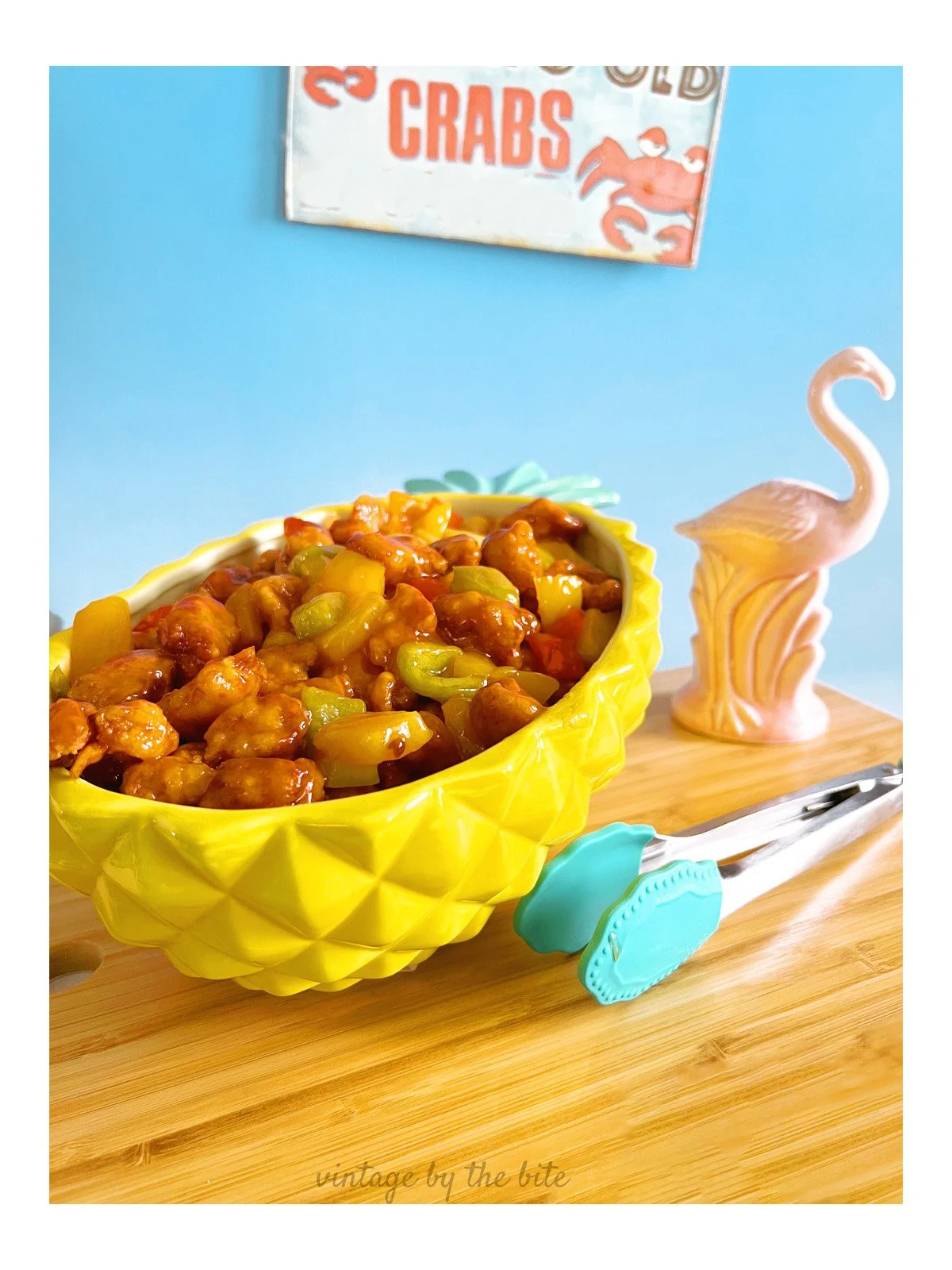 1970s-style sweet and sour chicken in a yellow pineapple bowl, topped with pineapple rings and colorful peppers, inspired by a vintage Don the Beachcomber recipe.
