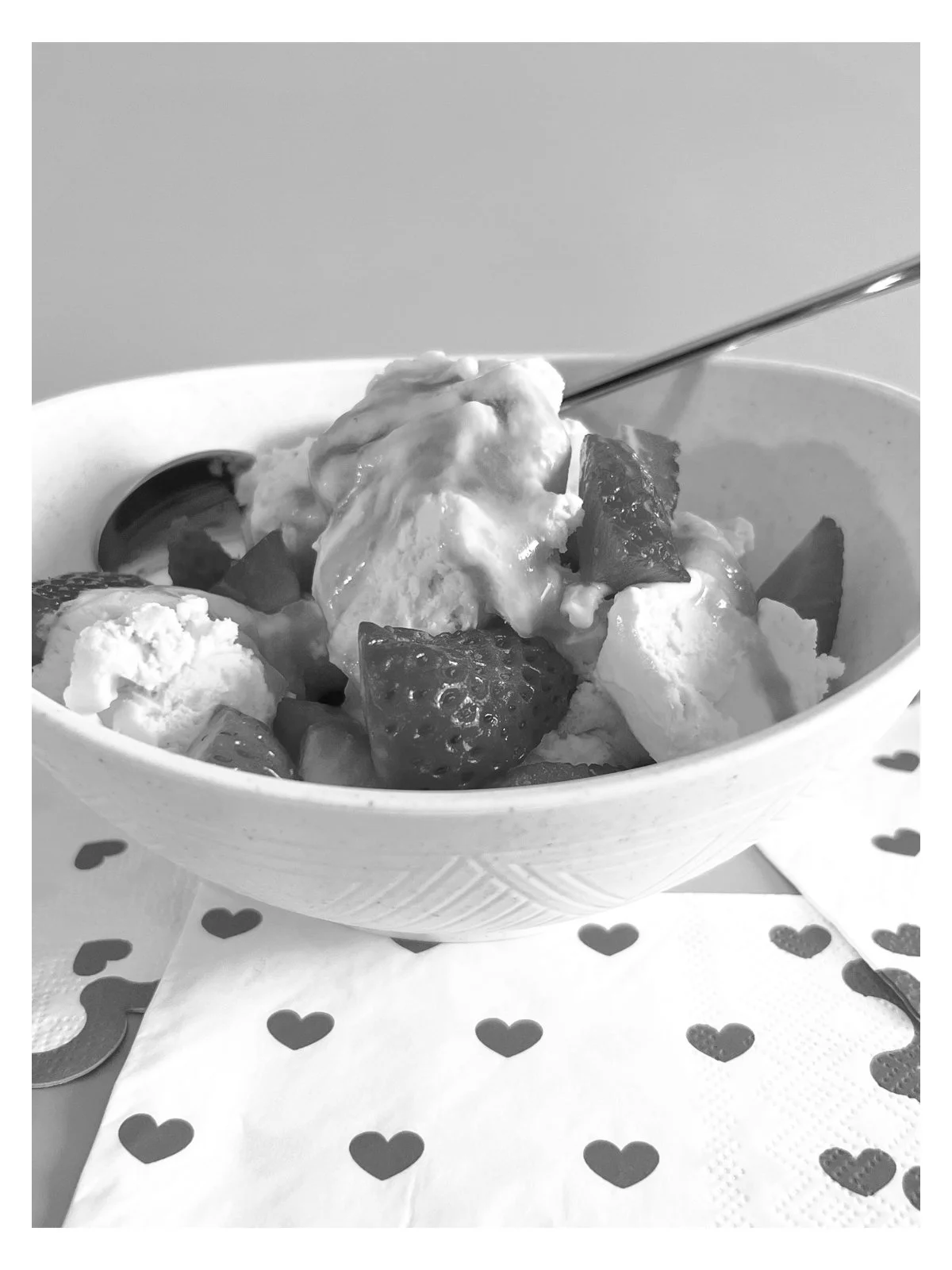 Black-and-white photo of vanilla ice cream topped with warm rum sauce and fresh strawberries in a white bowl