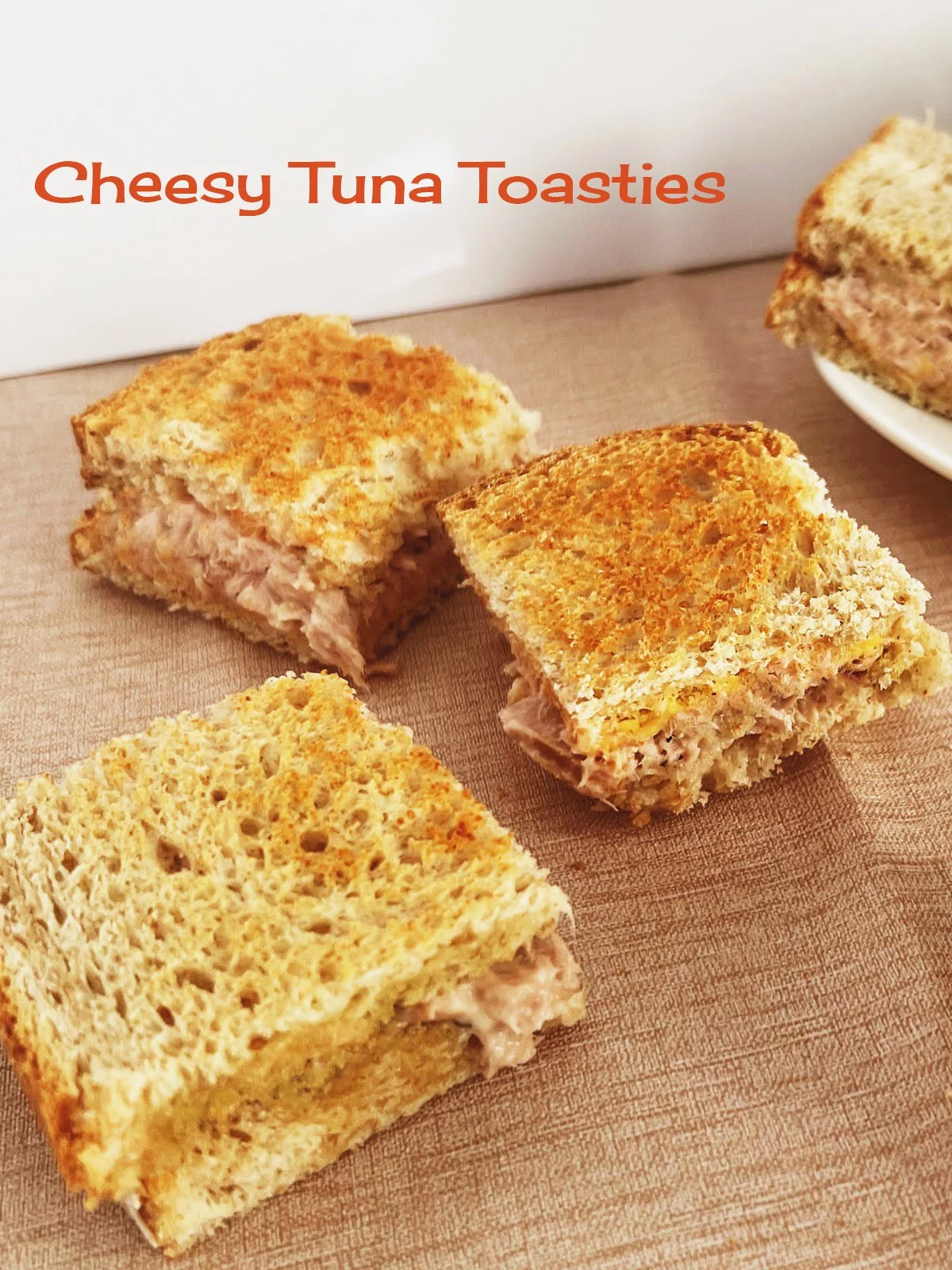 Golden toasted cheesy tuna toasties stacked and cut into quarters, featuring creamy tuna filling and melted Cheddar, a classic 1950s finger food recipe.