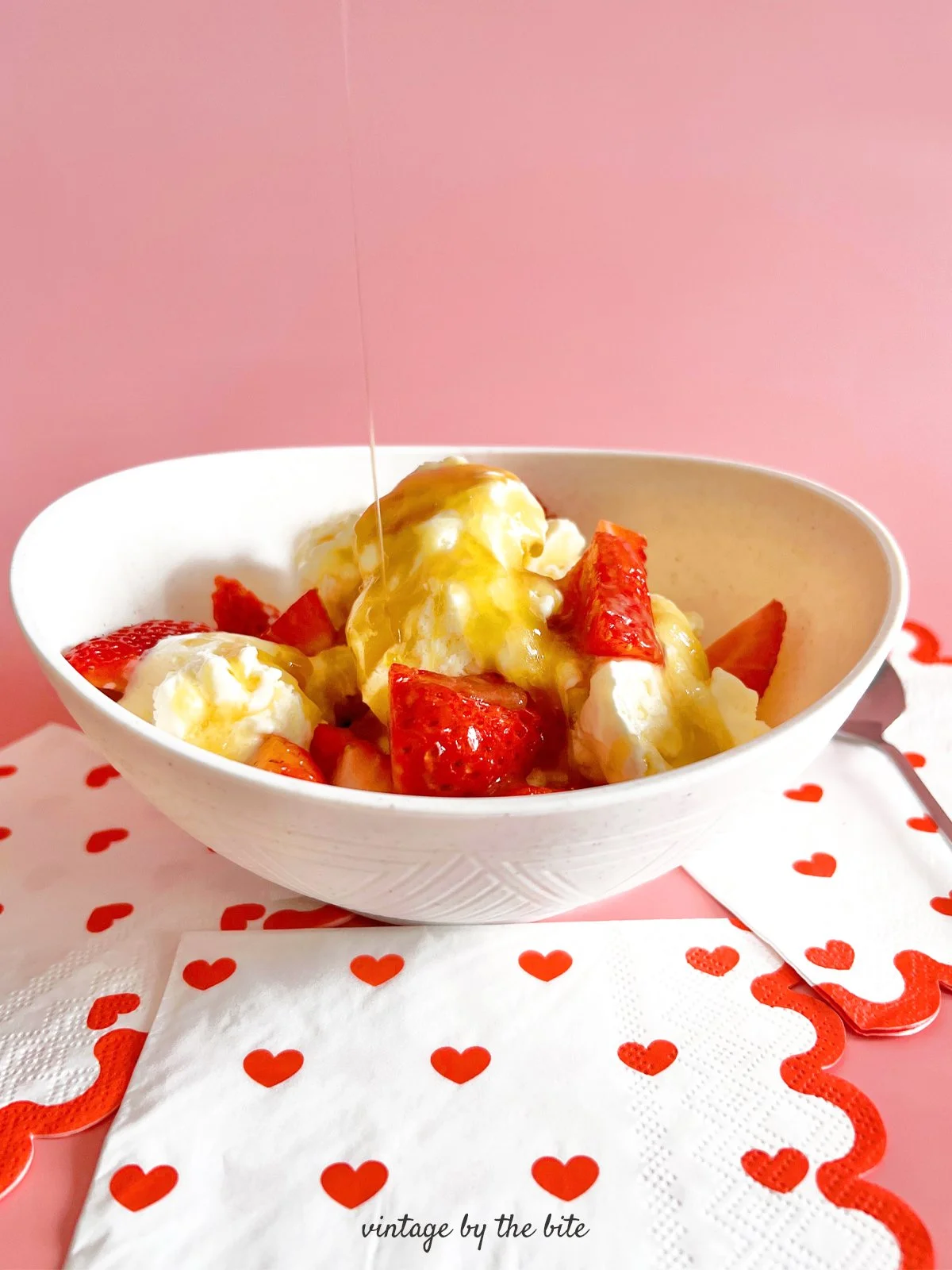 Vanilla ice cream topped with warm rum sauce and fresh strawberries in a white bowl,