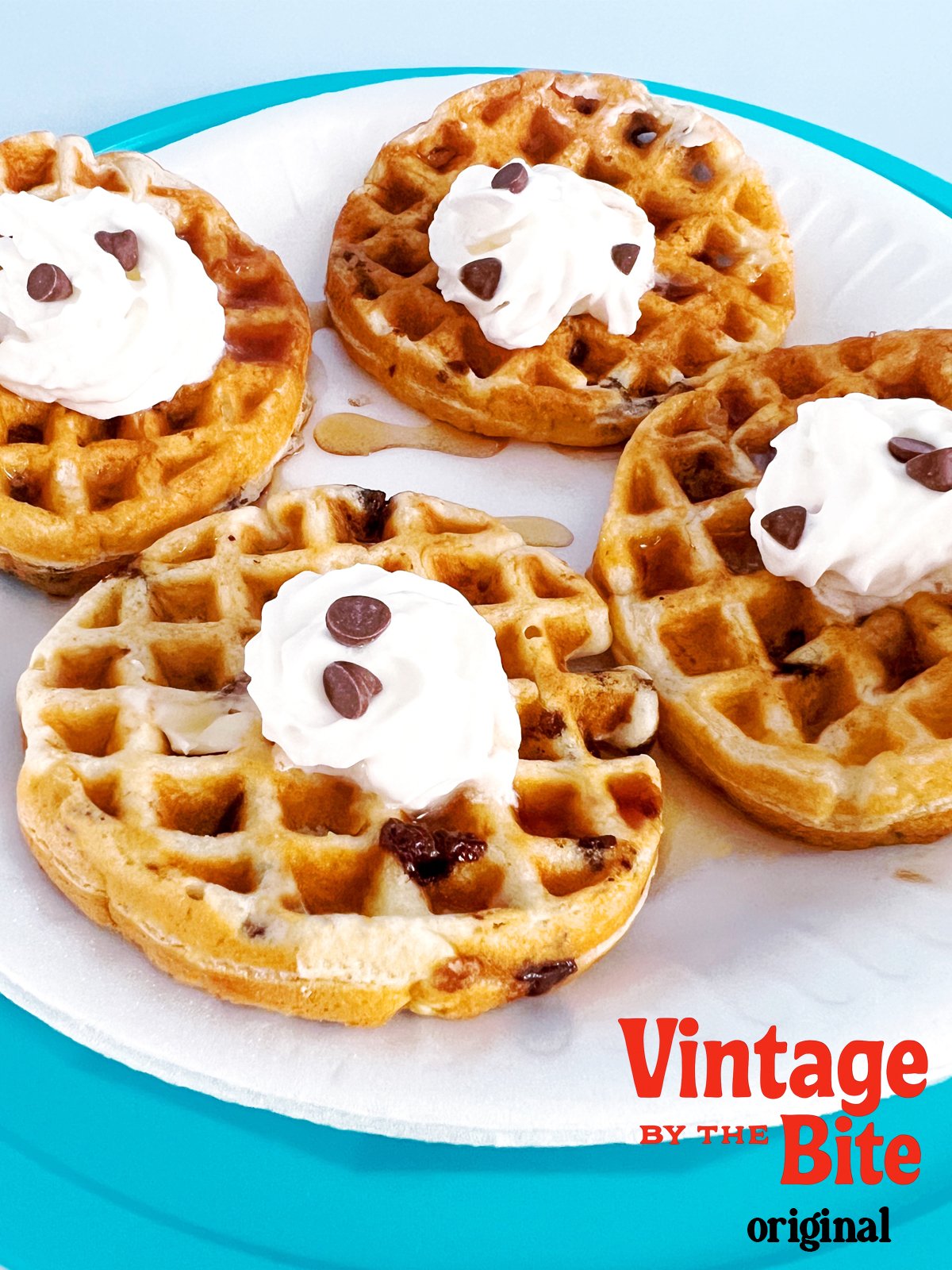 Four mini cappuccino chip waffles topped with whipped cream and chocolate chips on a white plate with a teal rim, with “Vintage by the Bite” branding in the corner.
