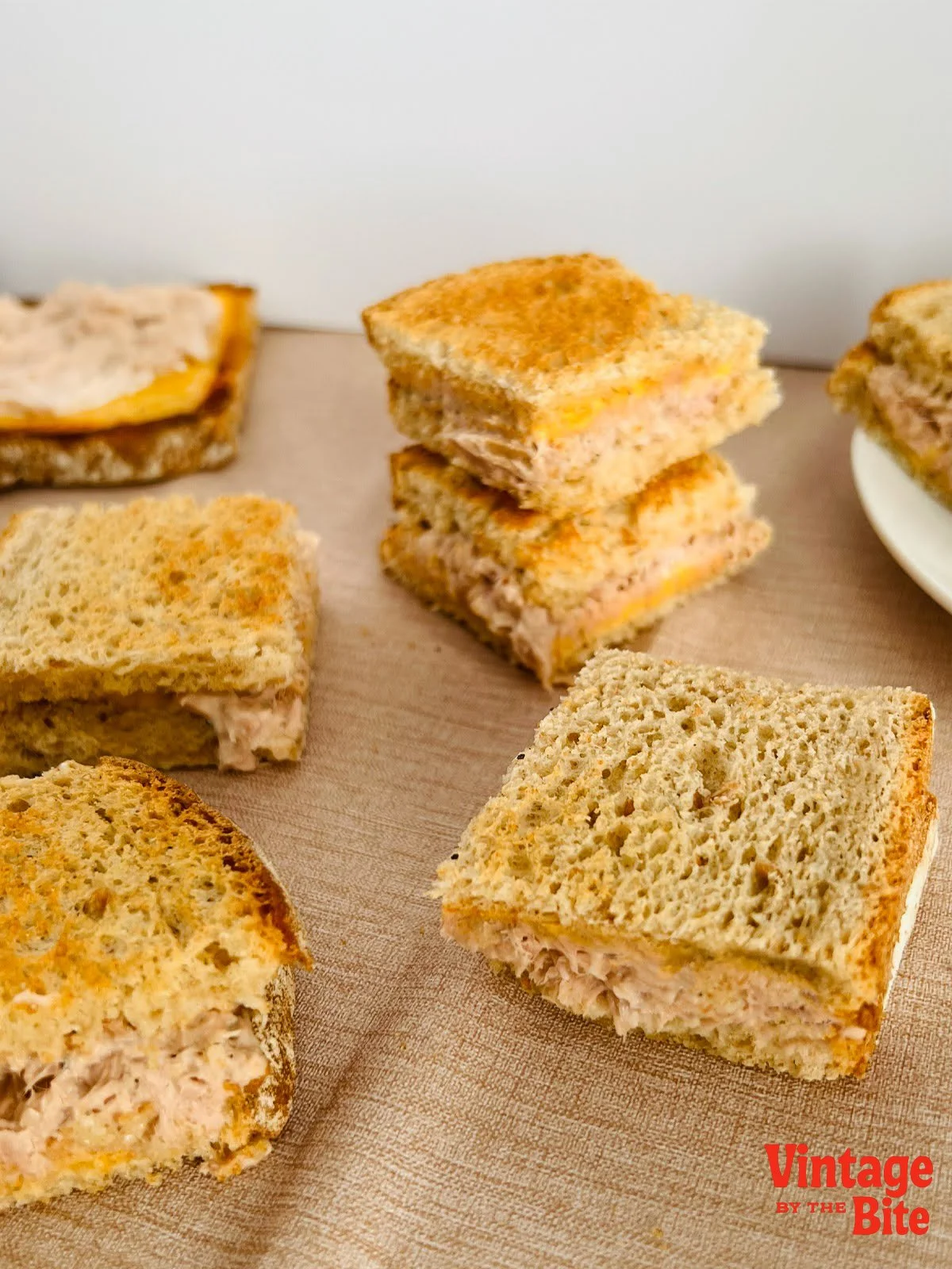 Golden toasted cheesy tuna toasties stacked and cut into quarters, featuring creamy tuna filling and melted Cheddar, a classic 1950s finger food recipe.
