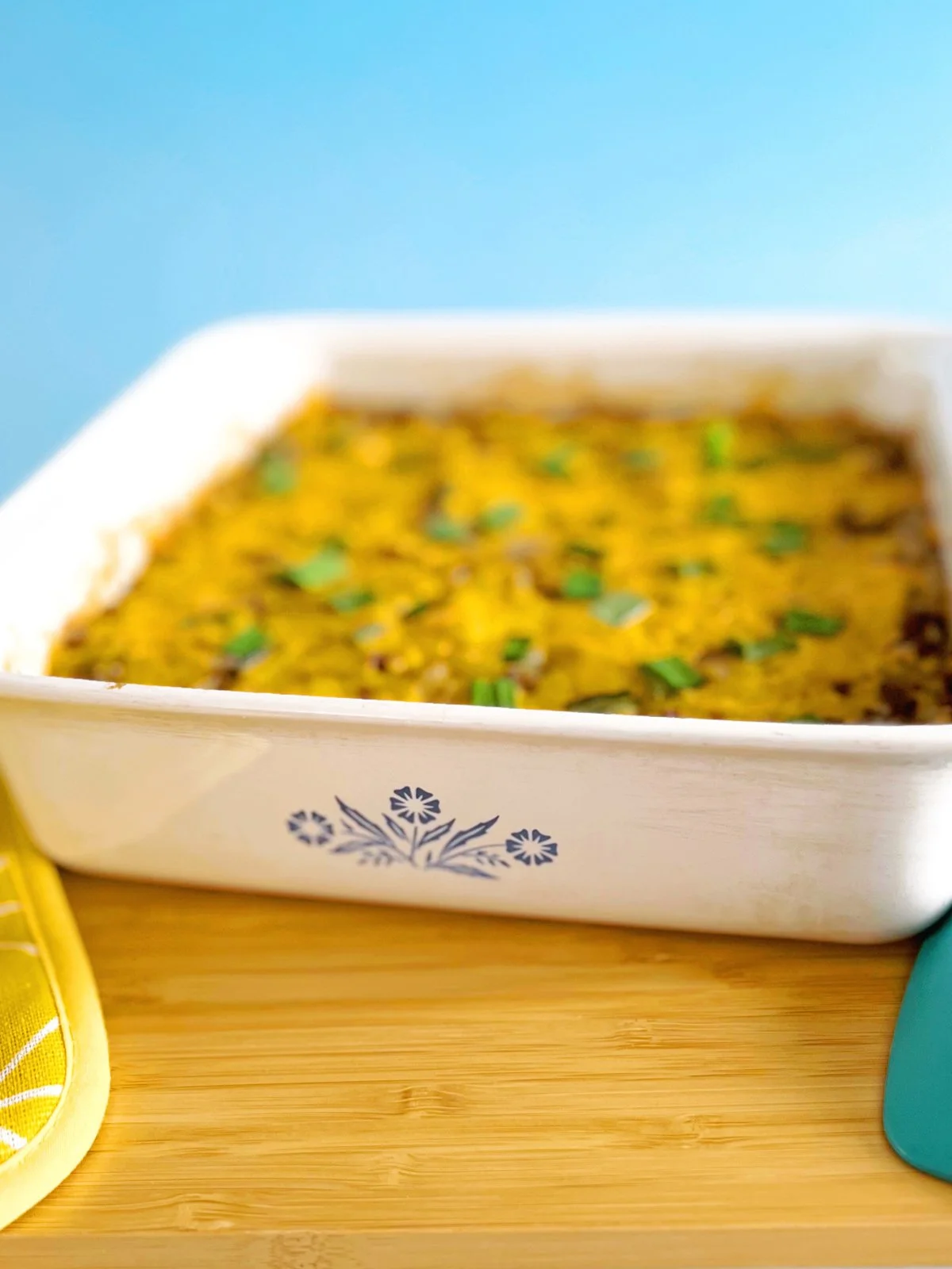 Old School Hamburger and Rice Casserole baked in a white vintage casserole dish with melted cheddar cheese and chopped green onions on top.