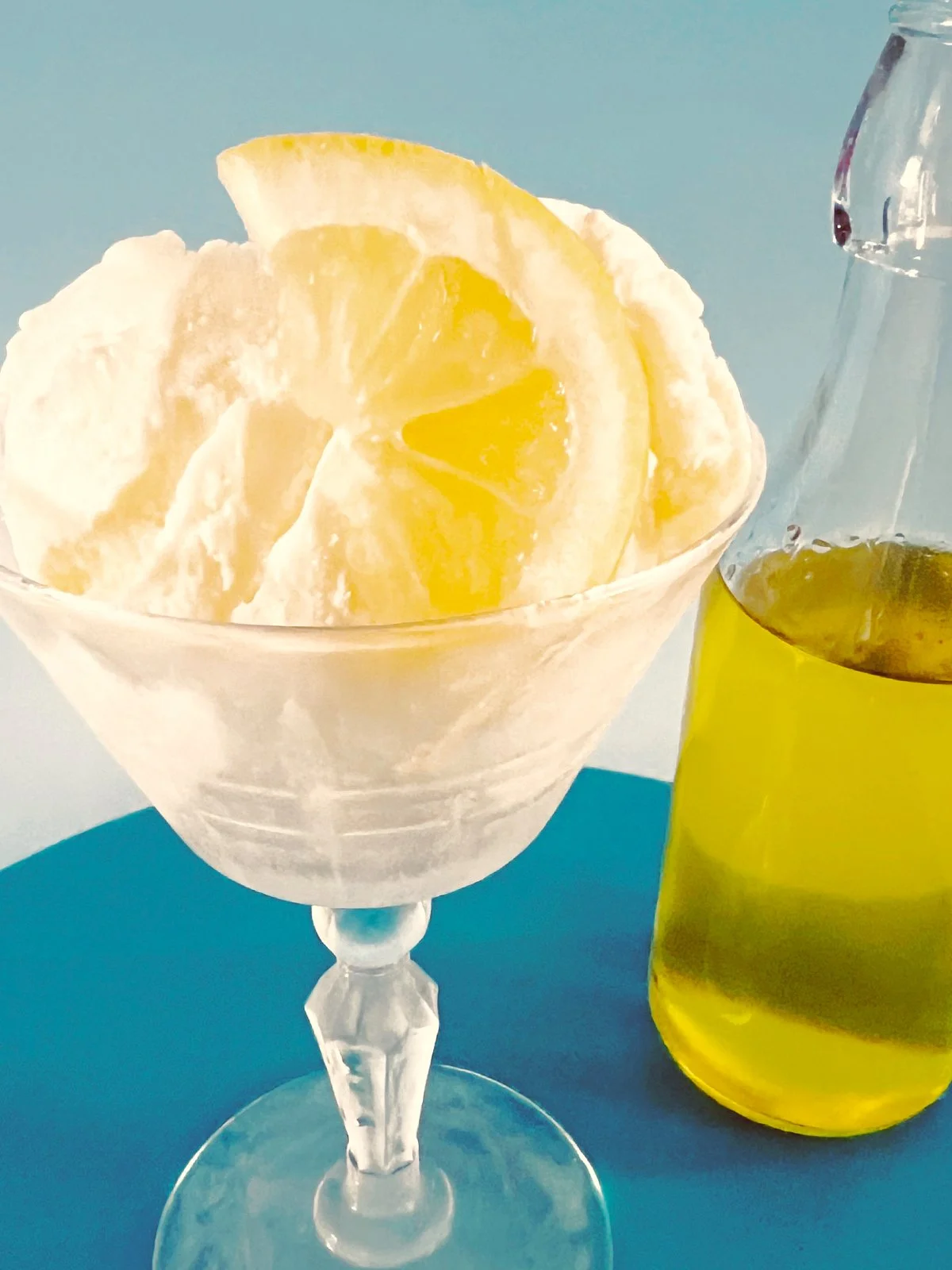 Vanilla ice cream in a vintage coupe glass topped with lemon slices and a drizzle of lemon syrup, with fresh lemons arranged around the base. - vintage look