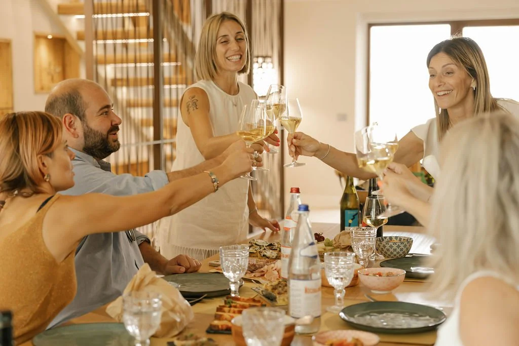 People celebrating with glasses of white wine around a dinner table indoors as part of an Oliver Oil Tasting.