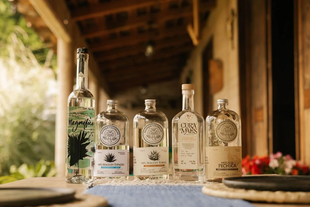 Five bottles of tequila on a table with a rustic background and some flowers in the background during a private mezcal experience. 