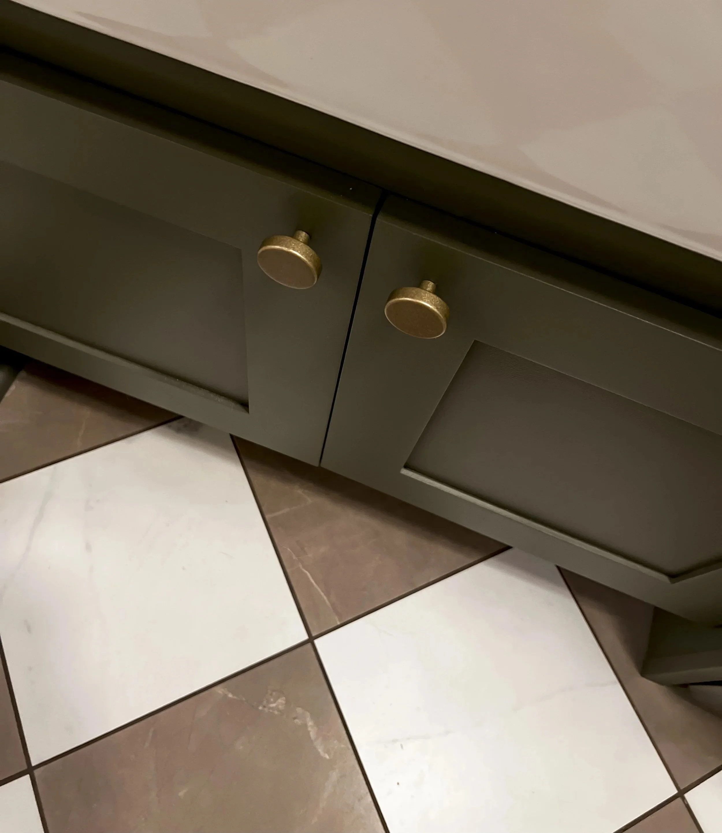 Interior design of an upscale laundry room for a Philadelphia area home. Embodying a modern yet timeless style, this space features dark olive custom cabinets, black granite counter above built-in laundry machines, and checker tile flooring.