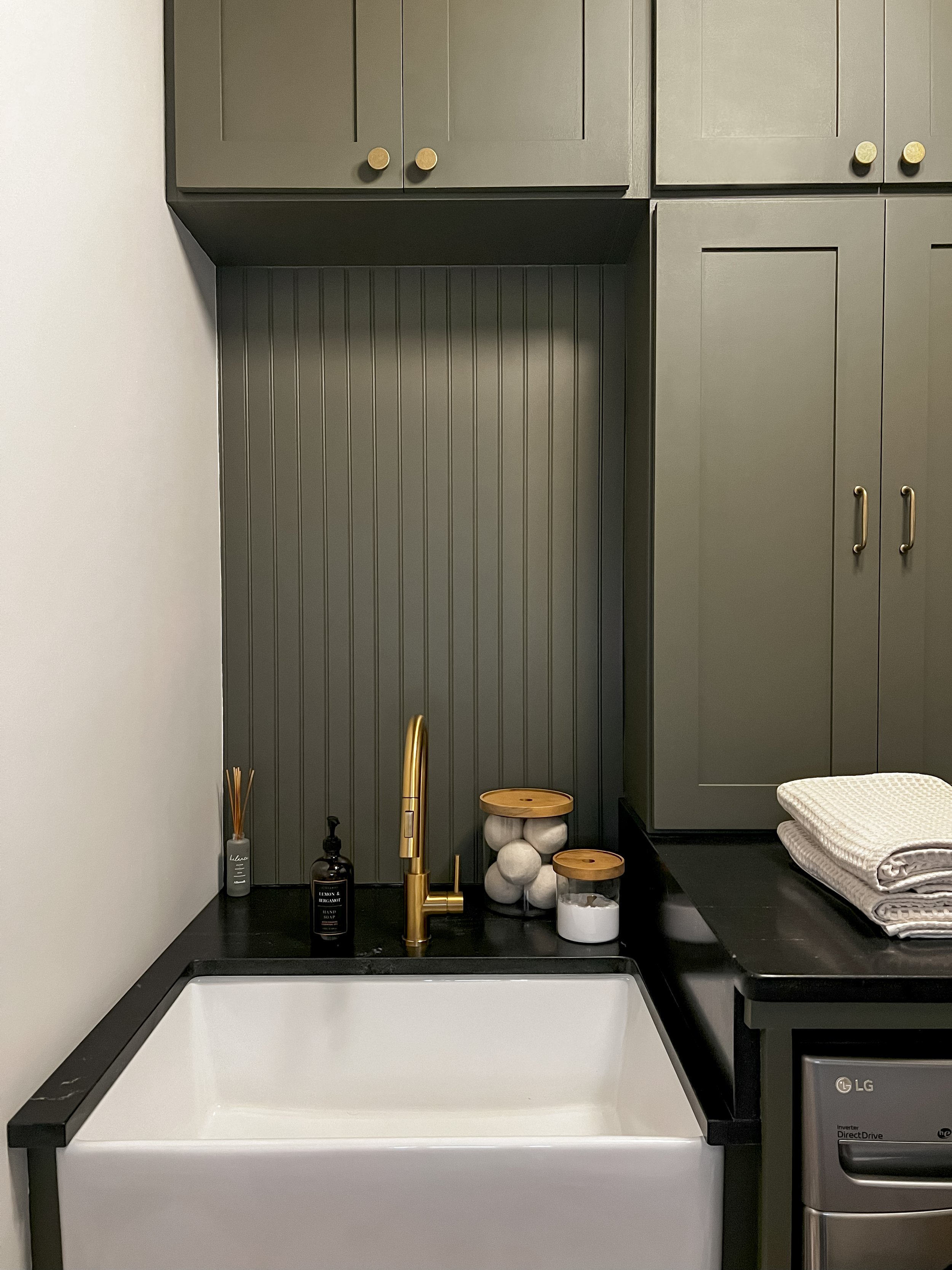 Interior design of an upscale laundry room for a Philadelphia area home. Embodying a modern yet timeless style, this space features dark olive custom cabinets, black granite counter above built-in laundry machines, and checker tile flooring.