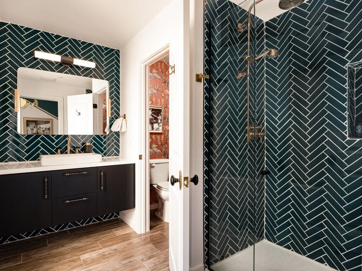 Modern bathroom with blue subway tiled shower area and vanity wall. Black vanity, large mirror, and brass fixtures.