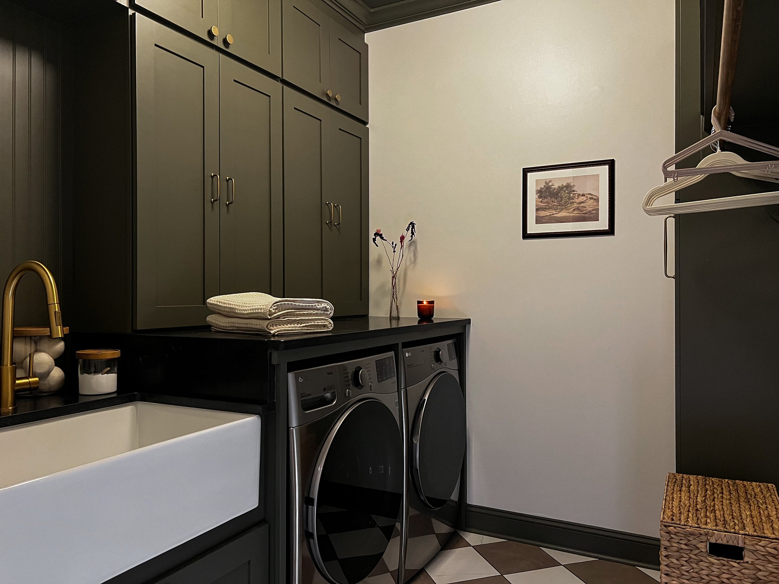 Interior design of an upscale laundry room for a Philadelphia area home. Embodying a modern yet timeless style, this space features dark olive custom cabinets, black granite counter above built-in laundry machines, and checker tile flooring.