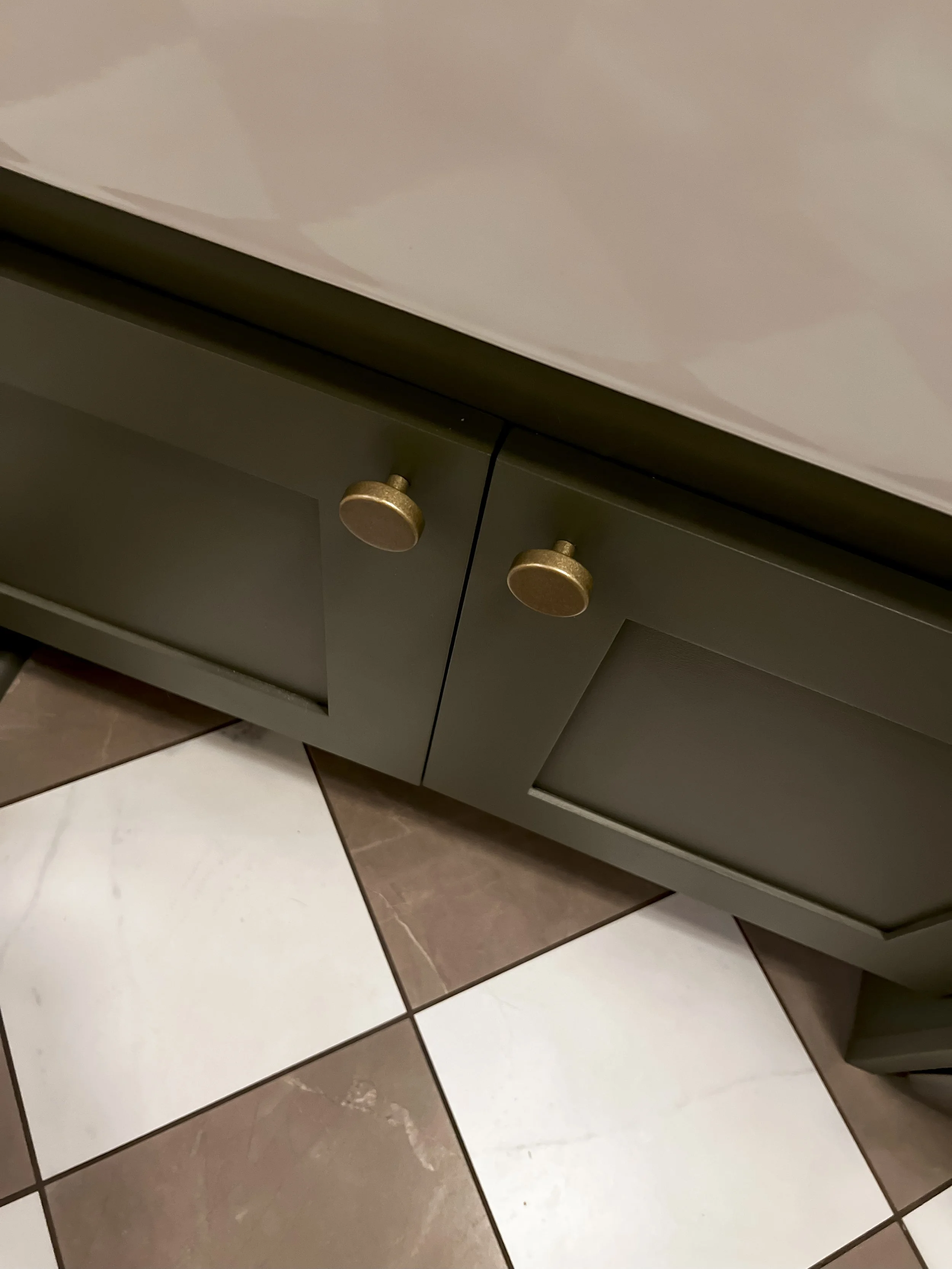Interior design of an upscale laundry room for a Philadelphia area home. Embodying a modern yet timeless style, this space features dark olive custom cabinets, black granite counter above built-in laundry machines, and checker tile flooring.