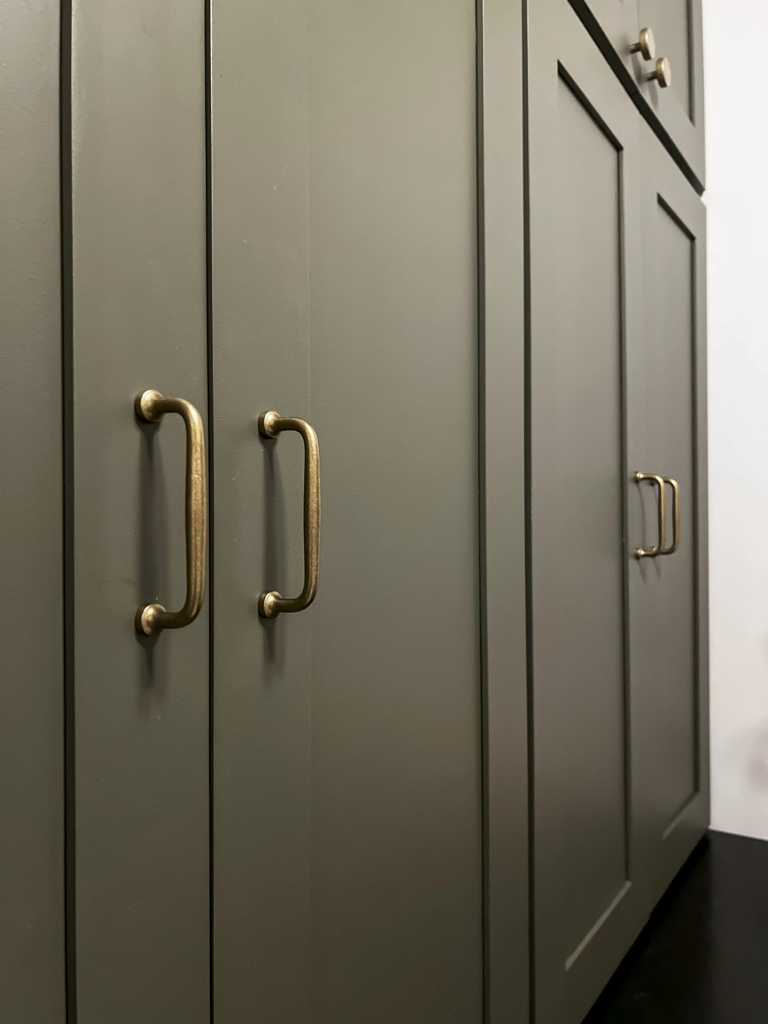 Interior design of an upscale laundry room for a Philadelphia area home. Embodying a modern yet timeless style, this space features dark olive custom cabinets, black granite counter above built-in laundry machines, and checker tile flooring.
