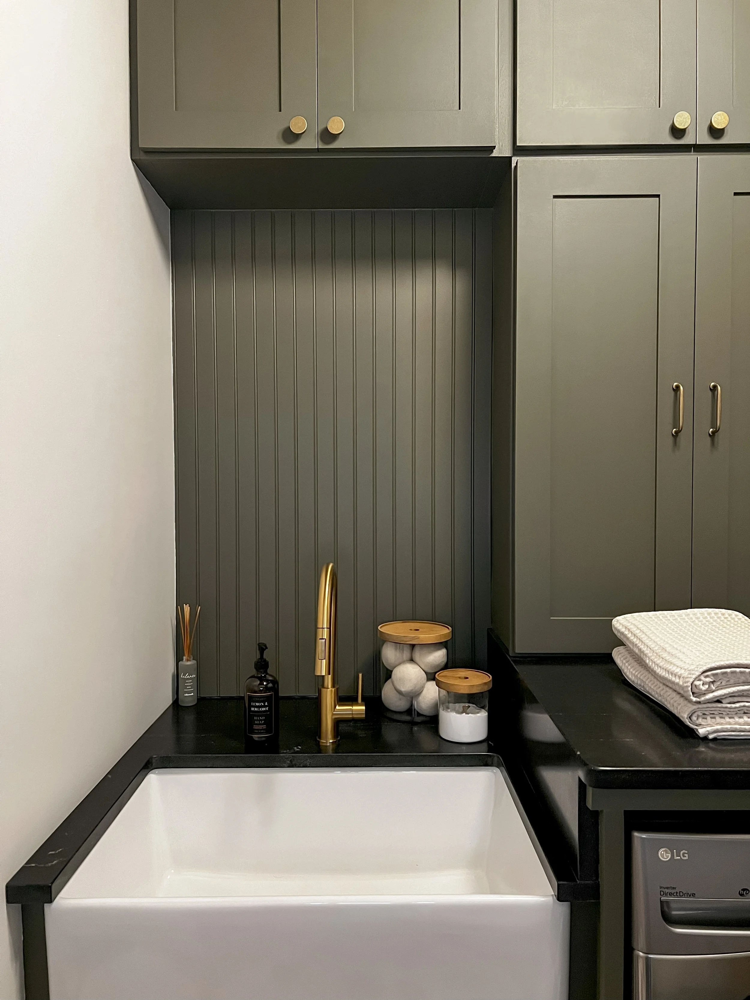 Interior design of an upscale laundry room for a Philadelphia area home. Embodying a modern yet timeless style, this space features dark olive custom cabinets, black granite counter above built-in laundry machines, and checker tile flooring.