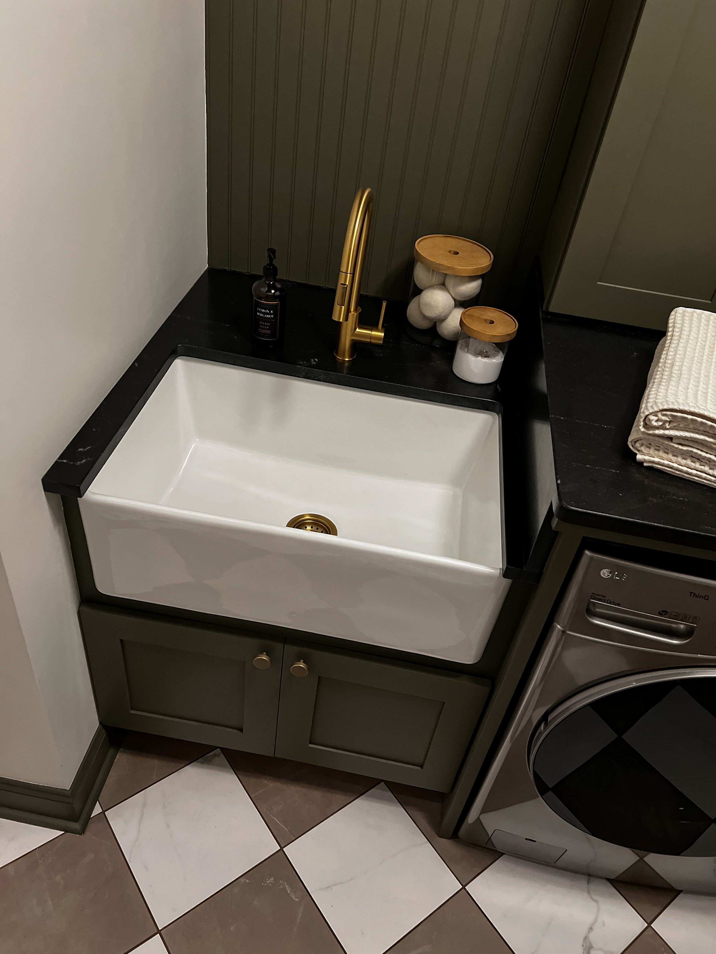 Interior design of an upscale laundry room for a Philadelphia area home. Embodying a modern yet timeless style, this space features dark olive custom cabinets, black granite counter above built-in laundry machines, and checker tile flooring.