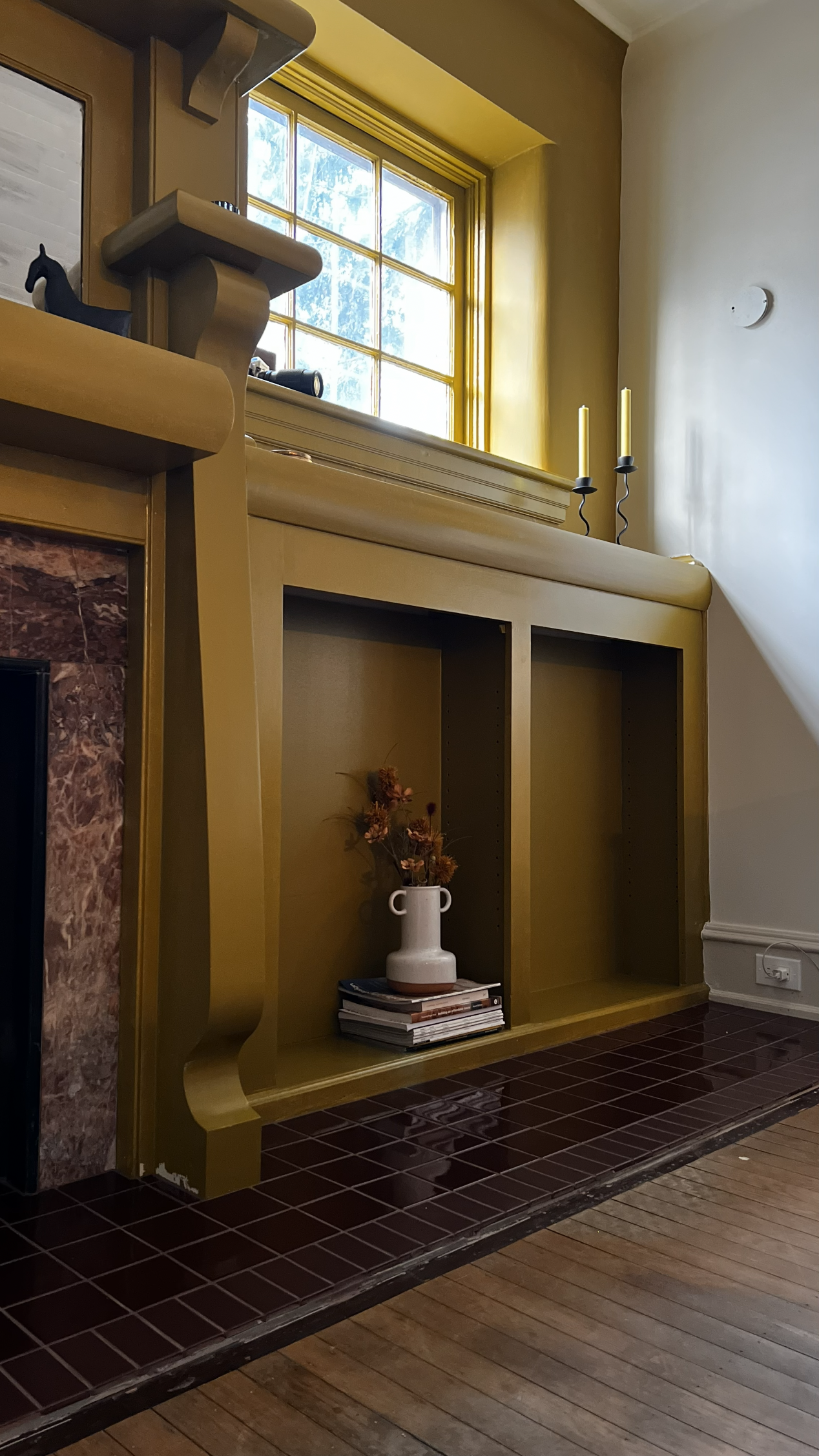 Fireplace and living room design featuring original built-ins and carpentry drenched in a bright yet saturated paint, rooted in an earthy aesthetic. A burgundy marble surrounding the firebox is original to the home, and was accentuated with new garne