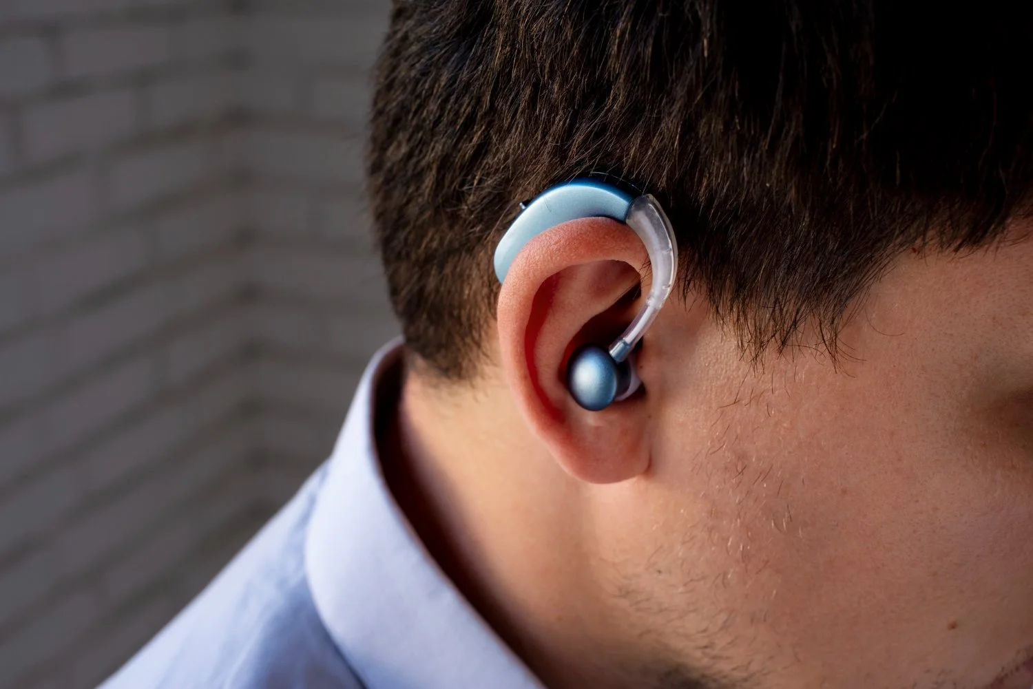 A man wearing a blue hearing aid in his right ear.