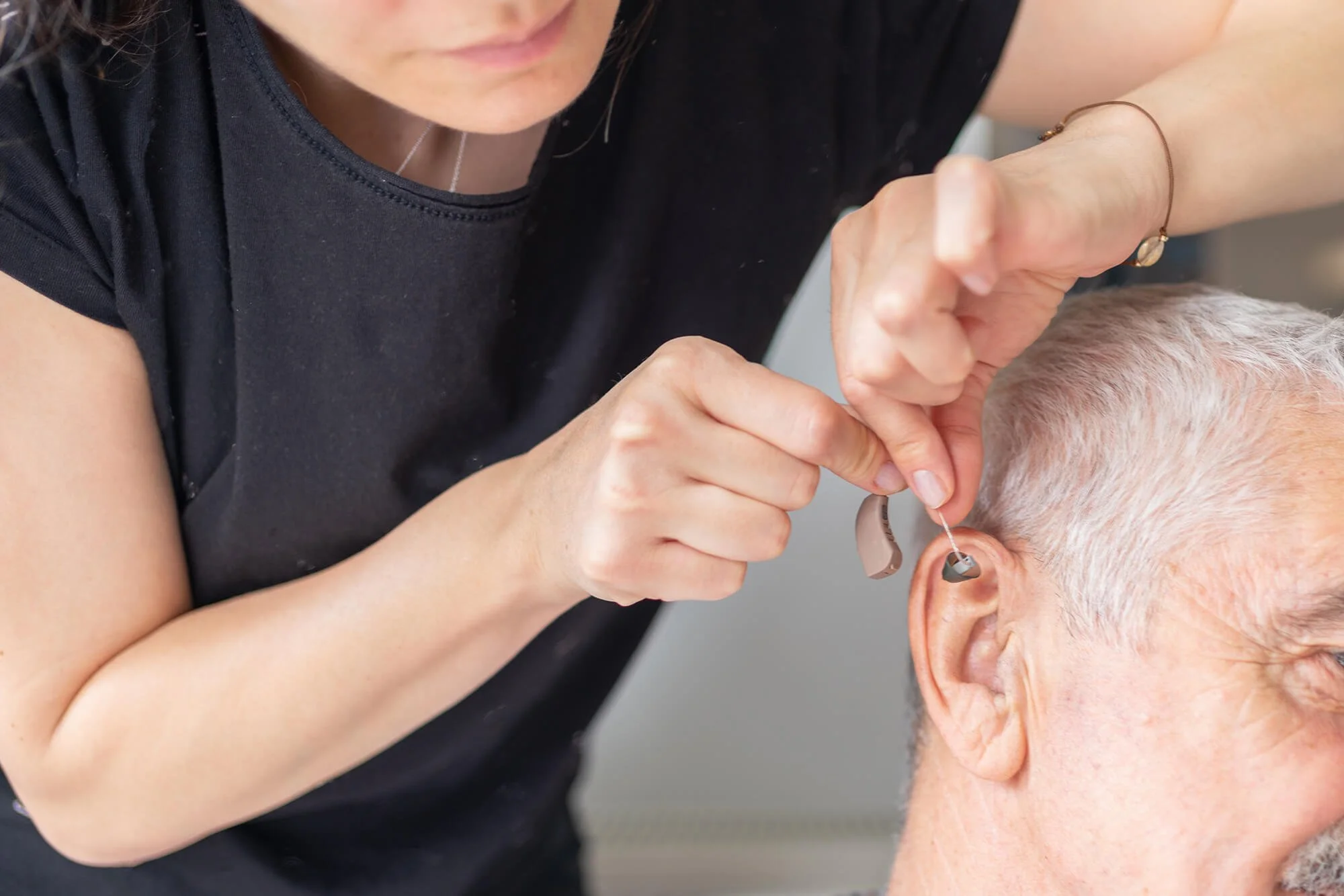 Audiologist fitting a hearing aid for a man's ear.