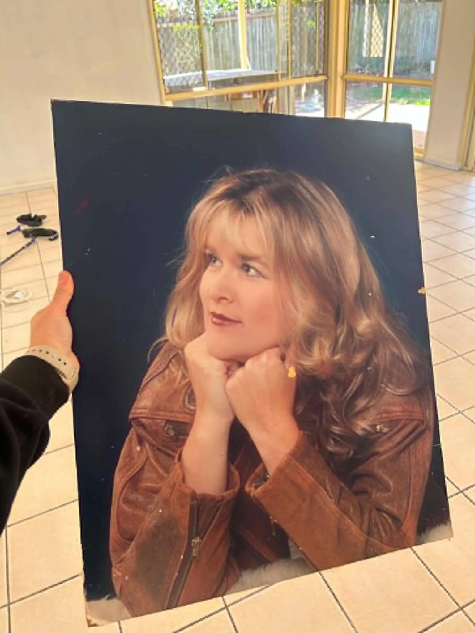Poster-sized glamour photograph from the 1990s showing a young woman with big hair and a leather jacket, being held up indoors.