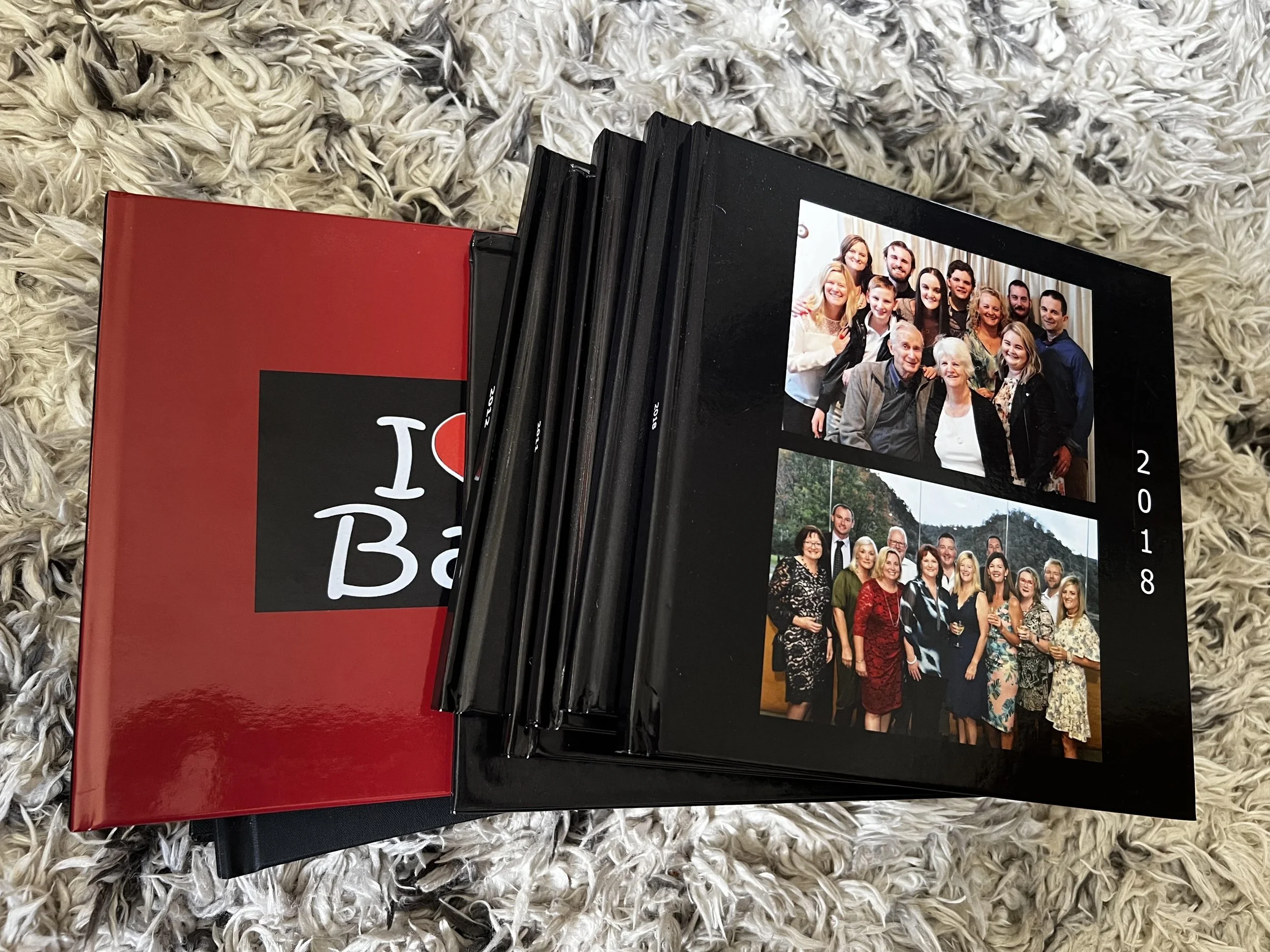Stack of black and red photo books on a rug, with family photographs visible on the top album.