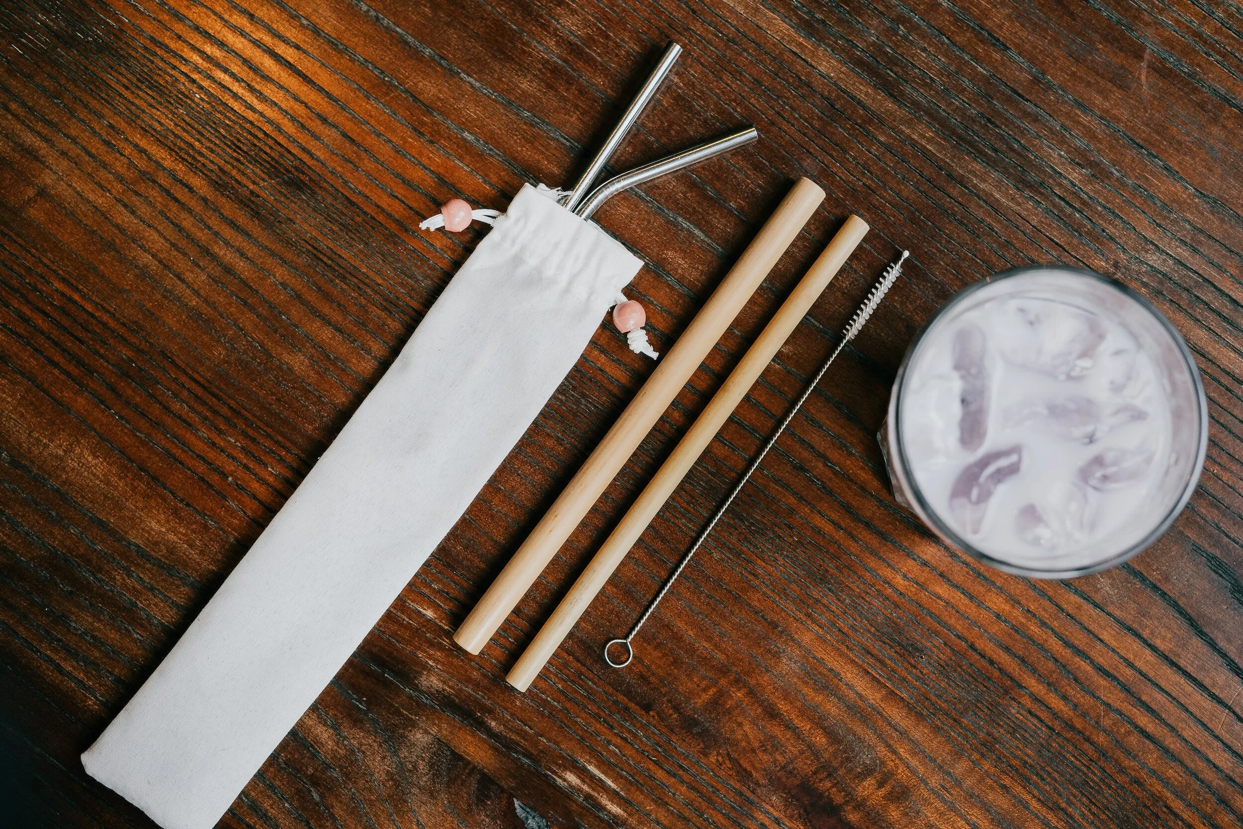 reusable straws of various sizes on table next to cup with ice cold beverage