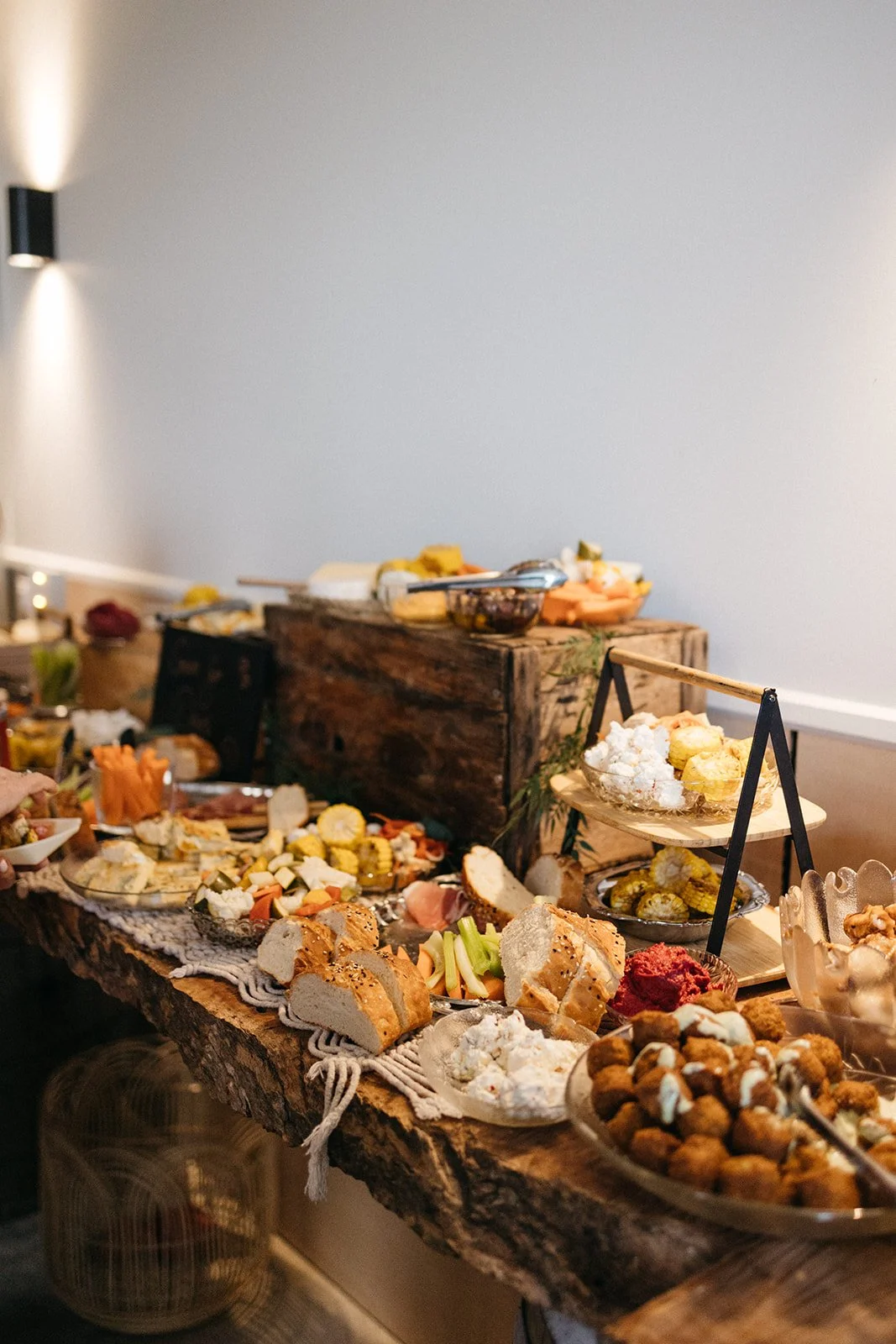 A rustic wooden table filled with various appetizers and finger foods, including bread, cheese, vegetables, and snacks, set up for a party or gathering.