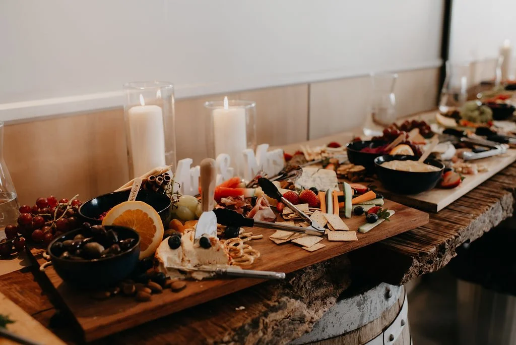 A cheese and fruit platter on a rustic wooden table with candles and glasses in the background.