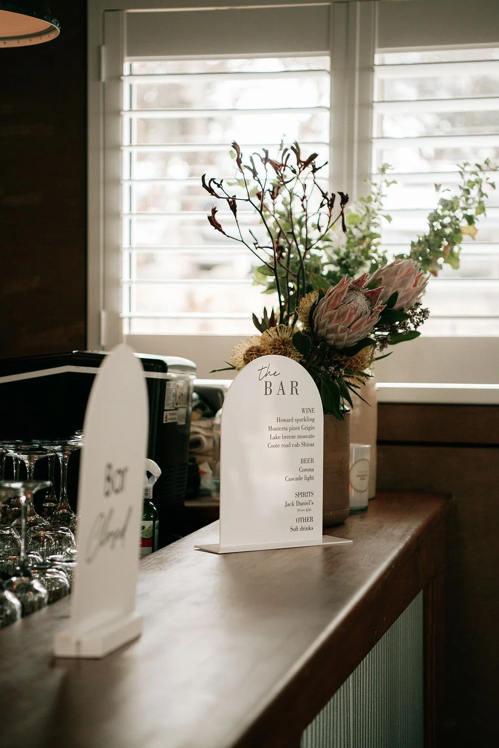 Bar counter with wine list menu and floral arrangement in front of window with white blinds.