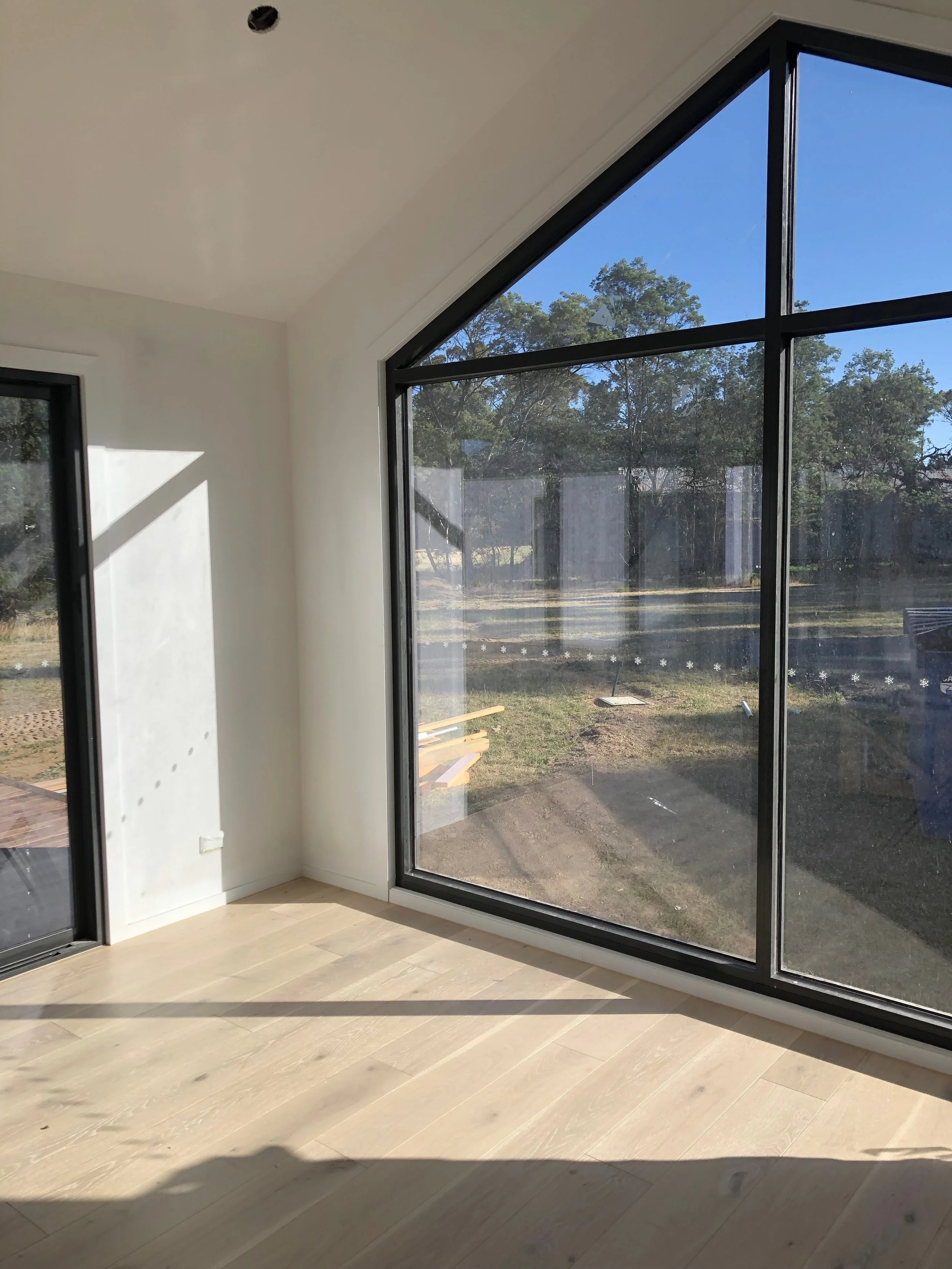 Empty room with large floor-to-ceiling windows showing outdoor trees and sky.