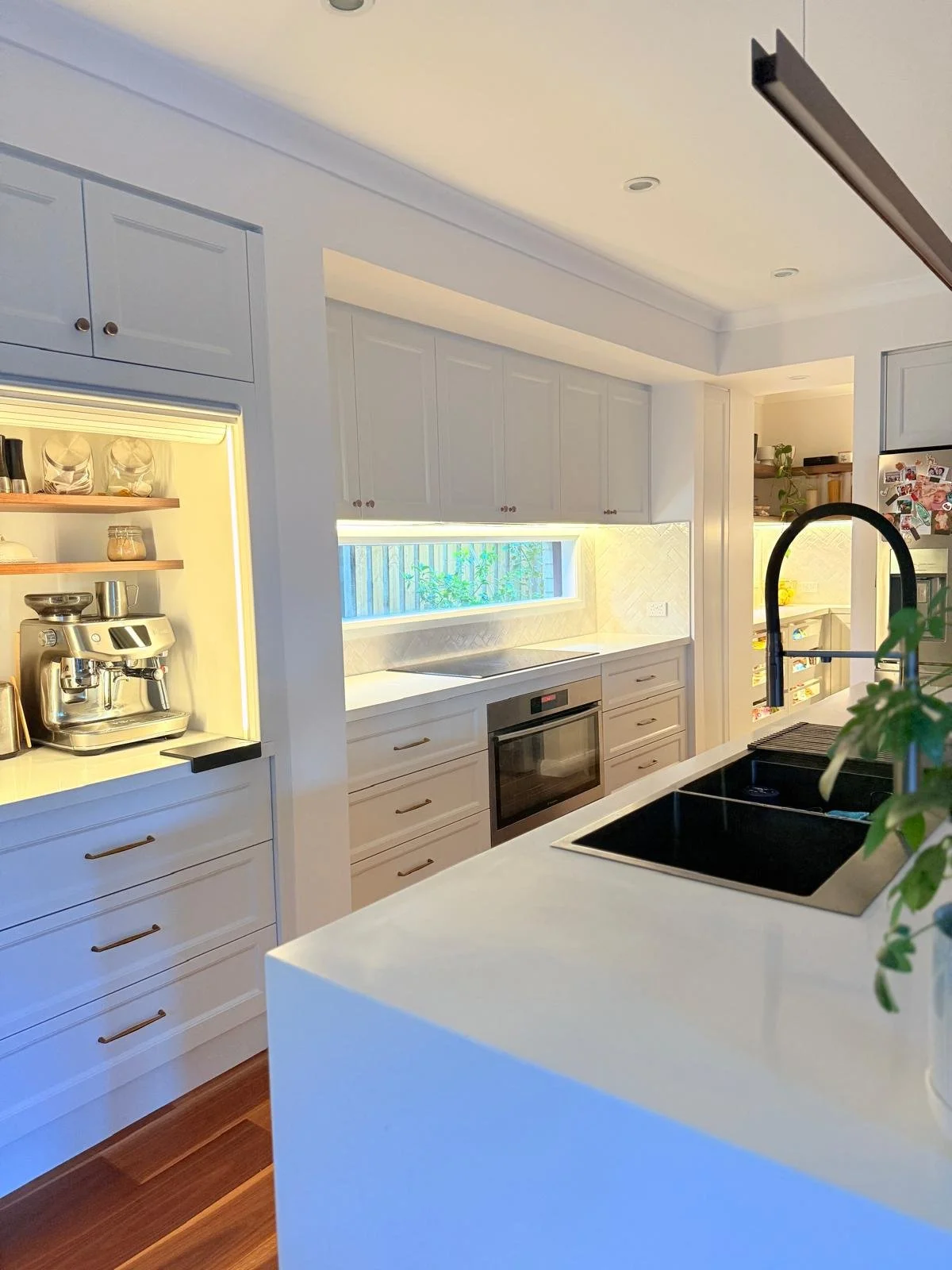 Modern kitchen with white cabinetry, black sink, built-in oven, coffee station, and a large window with natural light.