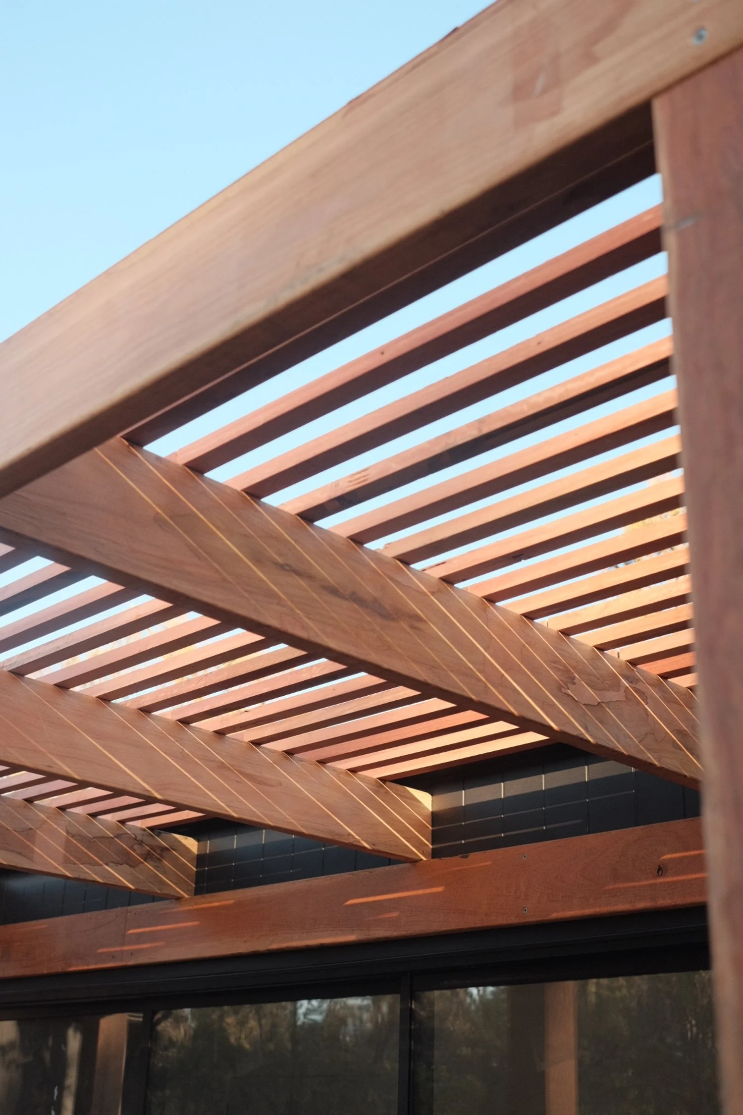 Close-up of a wooden porch roof with horizontal slats, viewed from below with clear blue sky in the background.