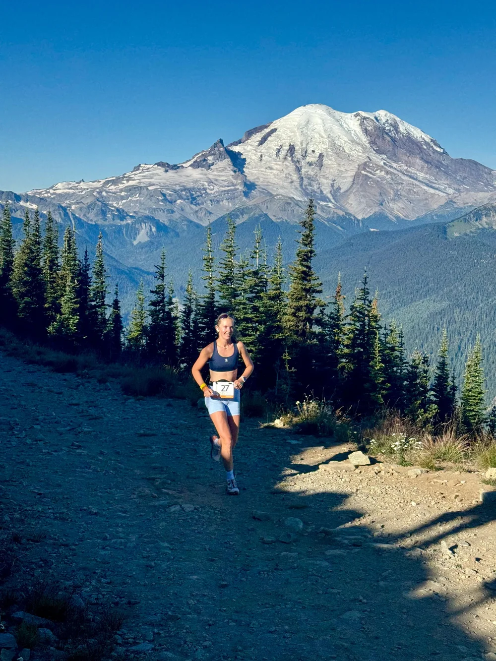 A racer in a bib running below a snow-covered peak