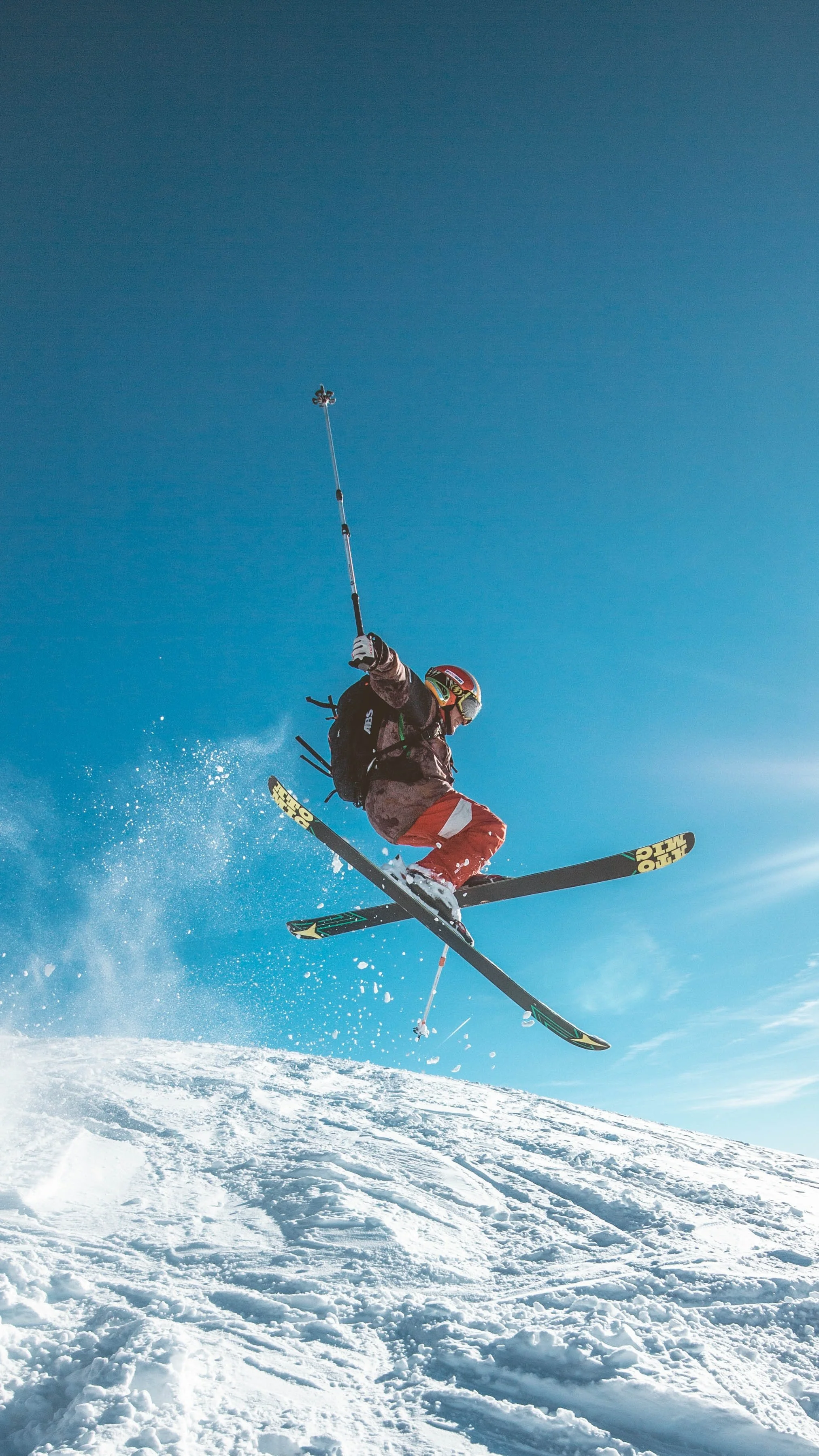 A skier in mid-air during a jump on a snowy slope under a clear blue sky.