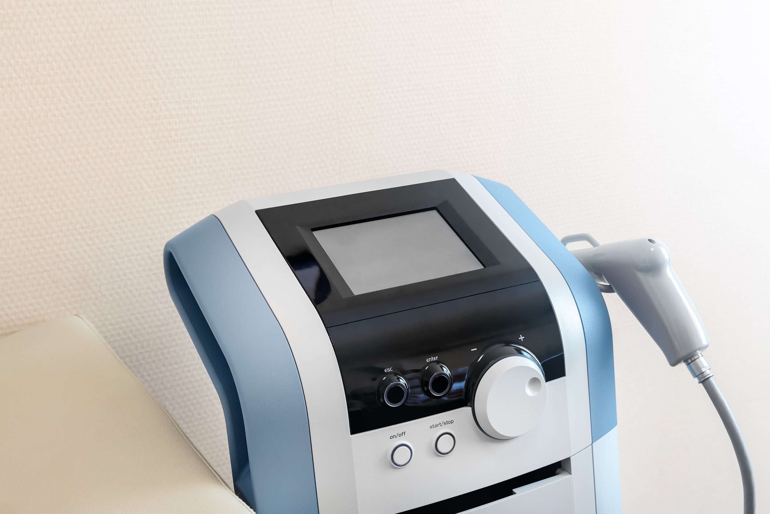 Medical laser device with a display screen and control knobs, connected to a handheld probe, against a light-colored wall.