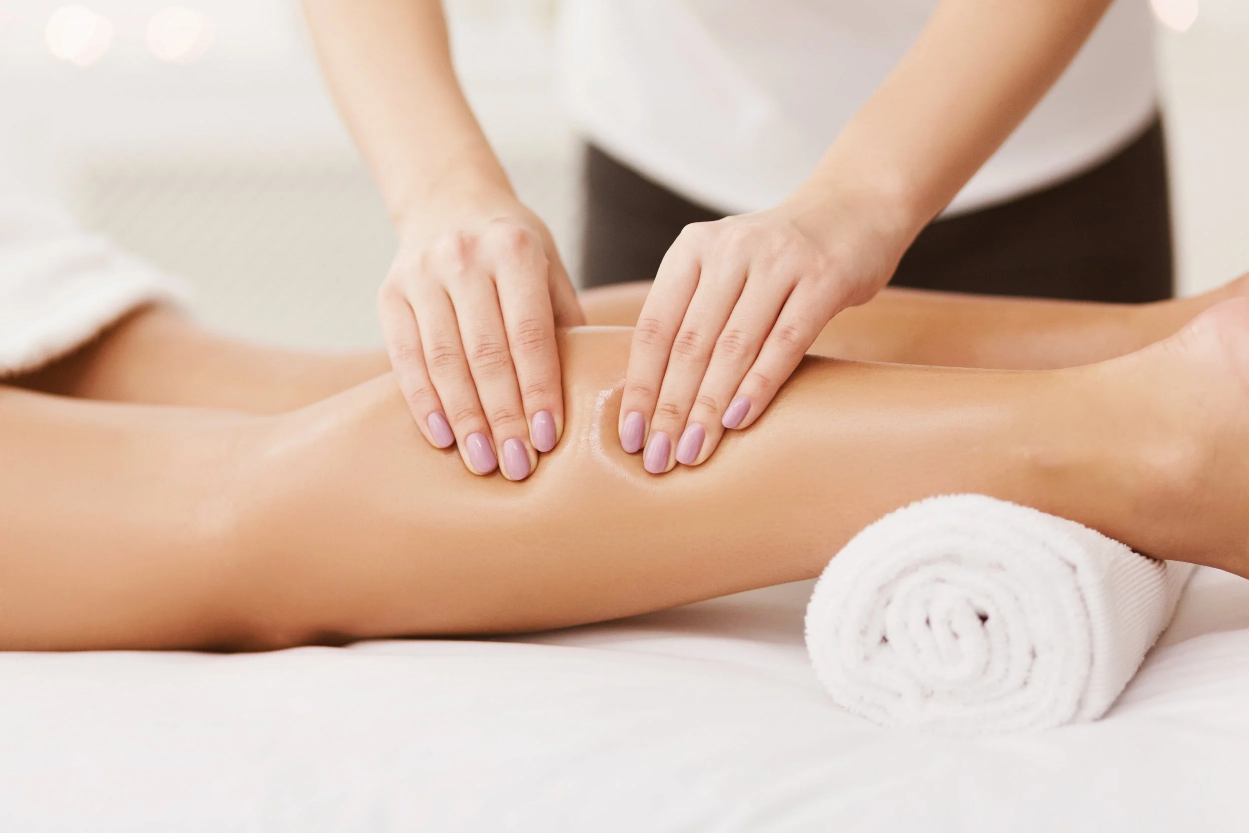 Person receiving a massage on their leg from a massage therapist in a spa setting.
